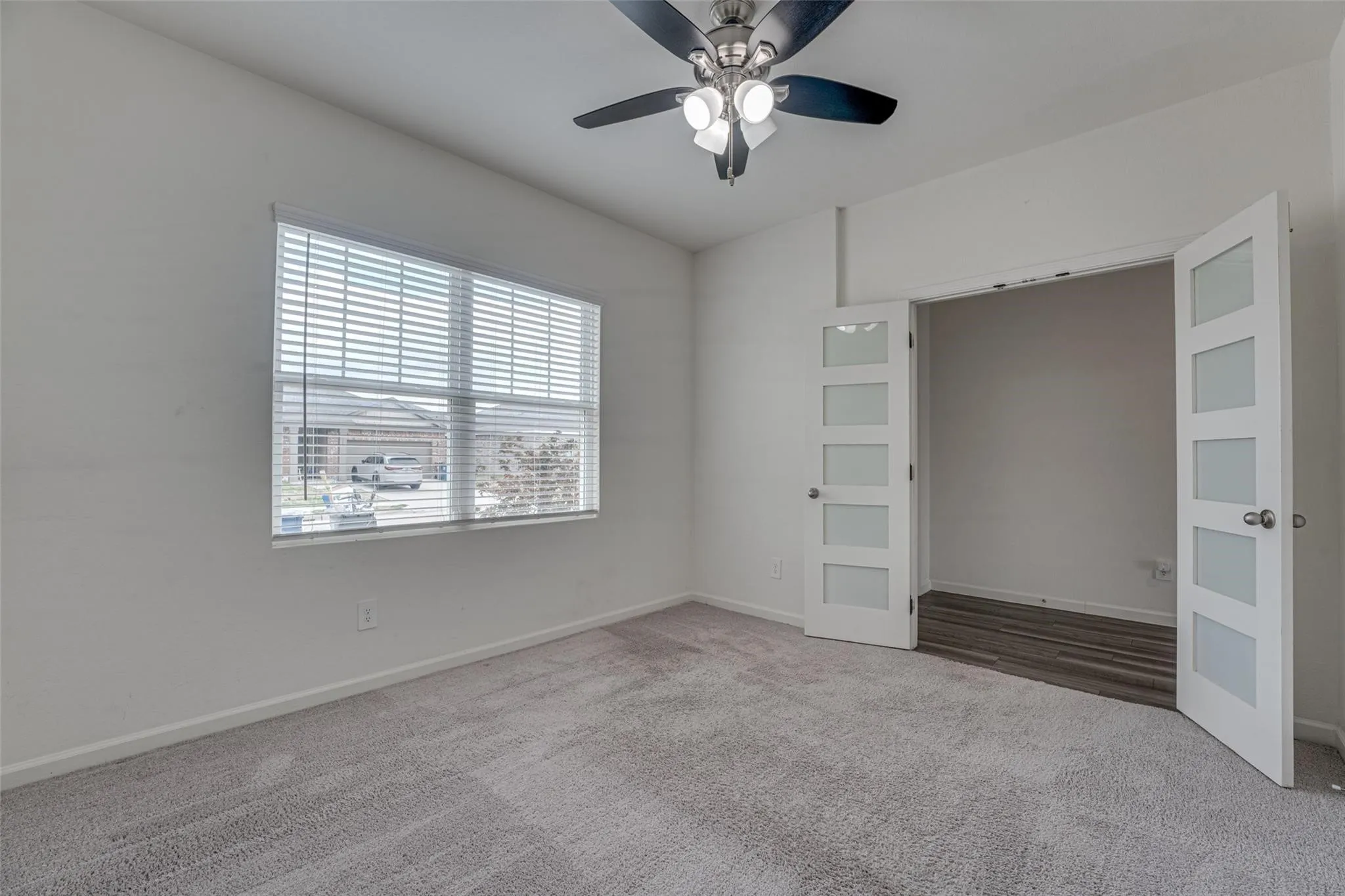 Light gray carpeted flooring, a ceiling fan with integrated lighting, and a window with horizontal blinds