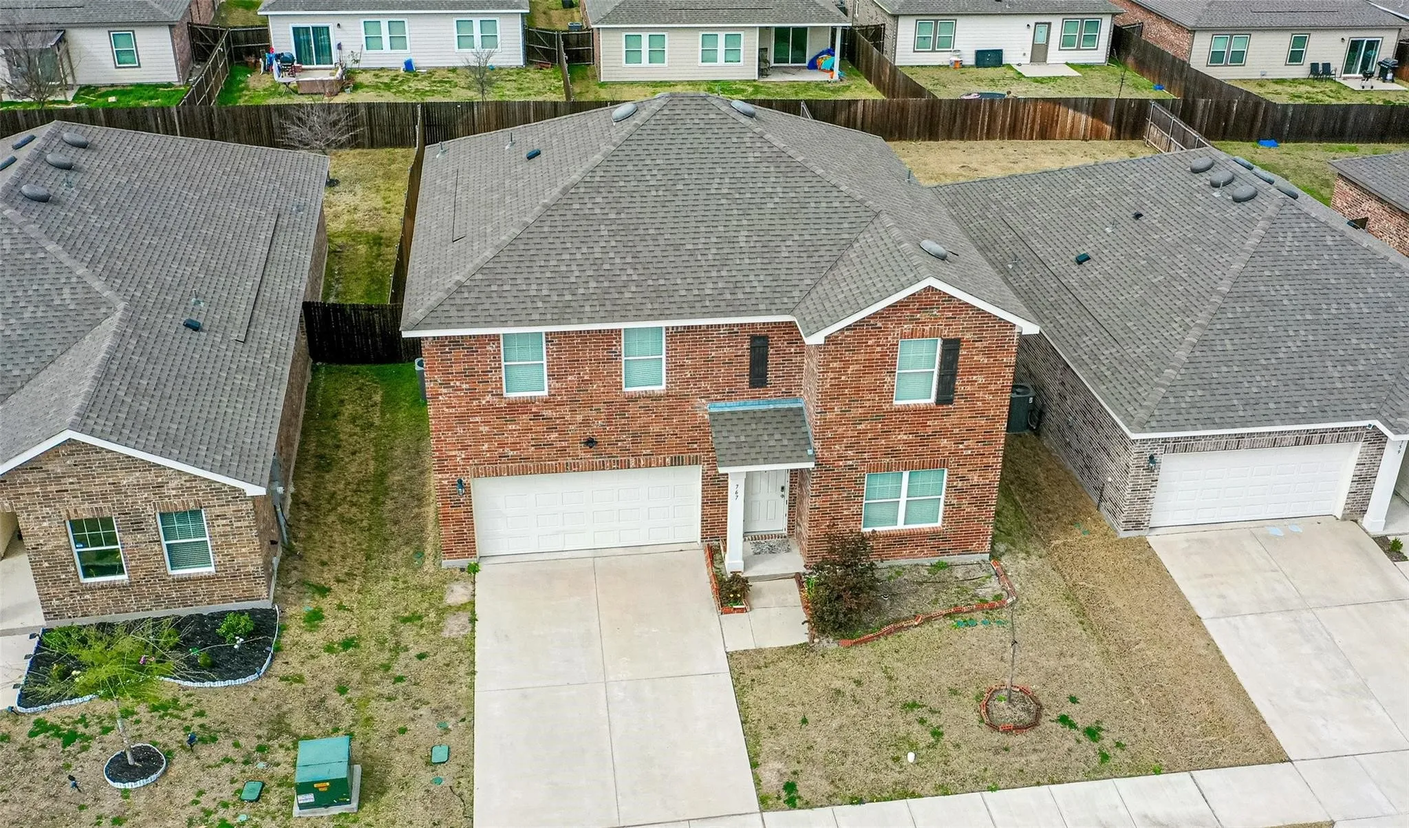Two-story brick exterior with a two-car garage, concrete driveway, and gray shingle roof