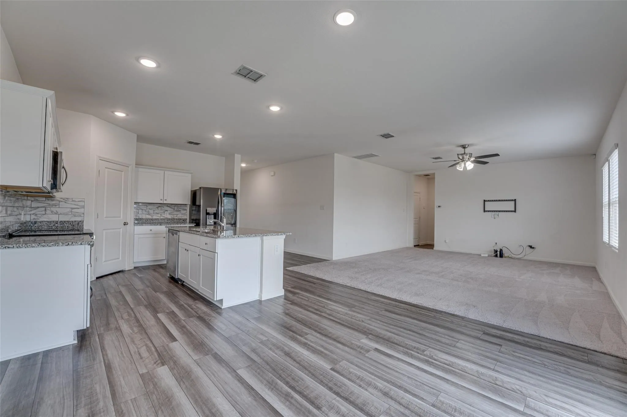 Open concept kitchen featuring white cabinetry, a kitchen island, stainless steel appliances, and wood-finish flooring