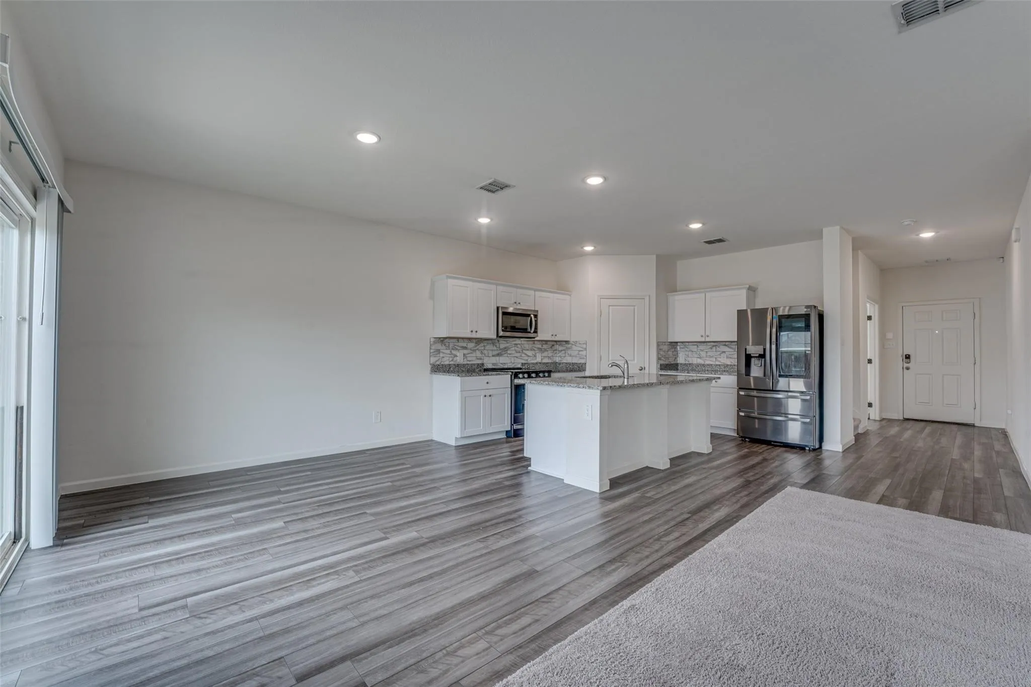 Open-concept living space featuring wood-finish flooring, recessed lighting, and a sliding glass door