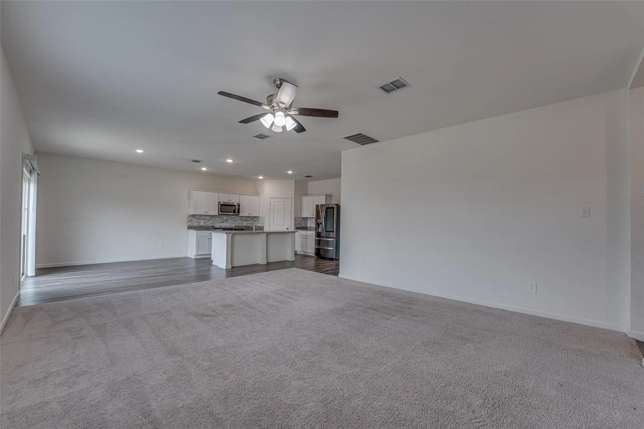 Spacious open-concept living area featuring soft gray carpeting, wood-finish flooring, a ceiling fan, and recessed lighting