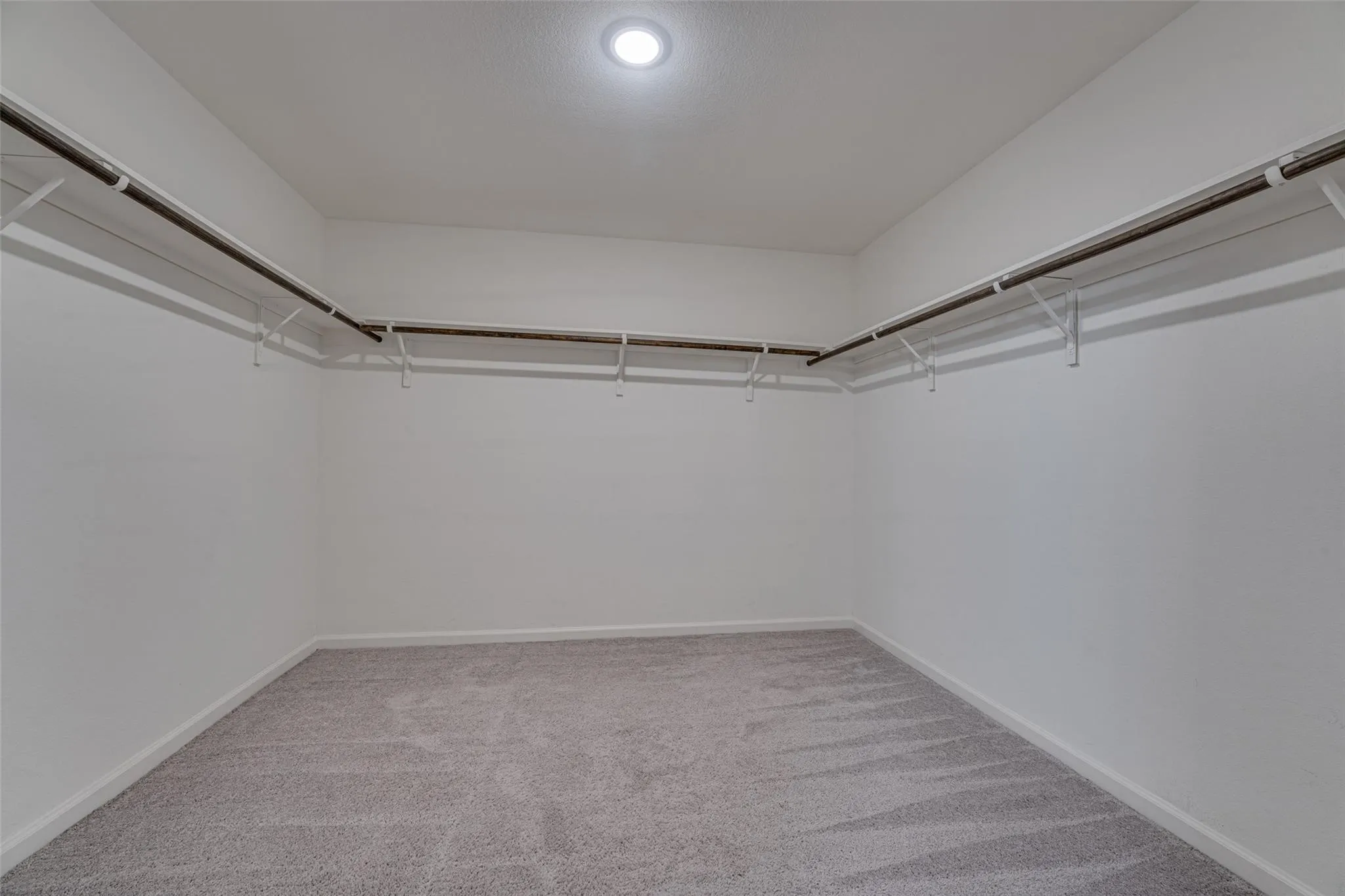 Recessed ceiling lighting, wall-mounted hanging rods, wire shelving, light grey carpeting, and neutral wall paint