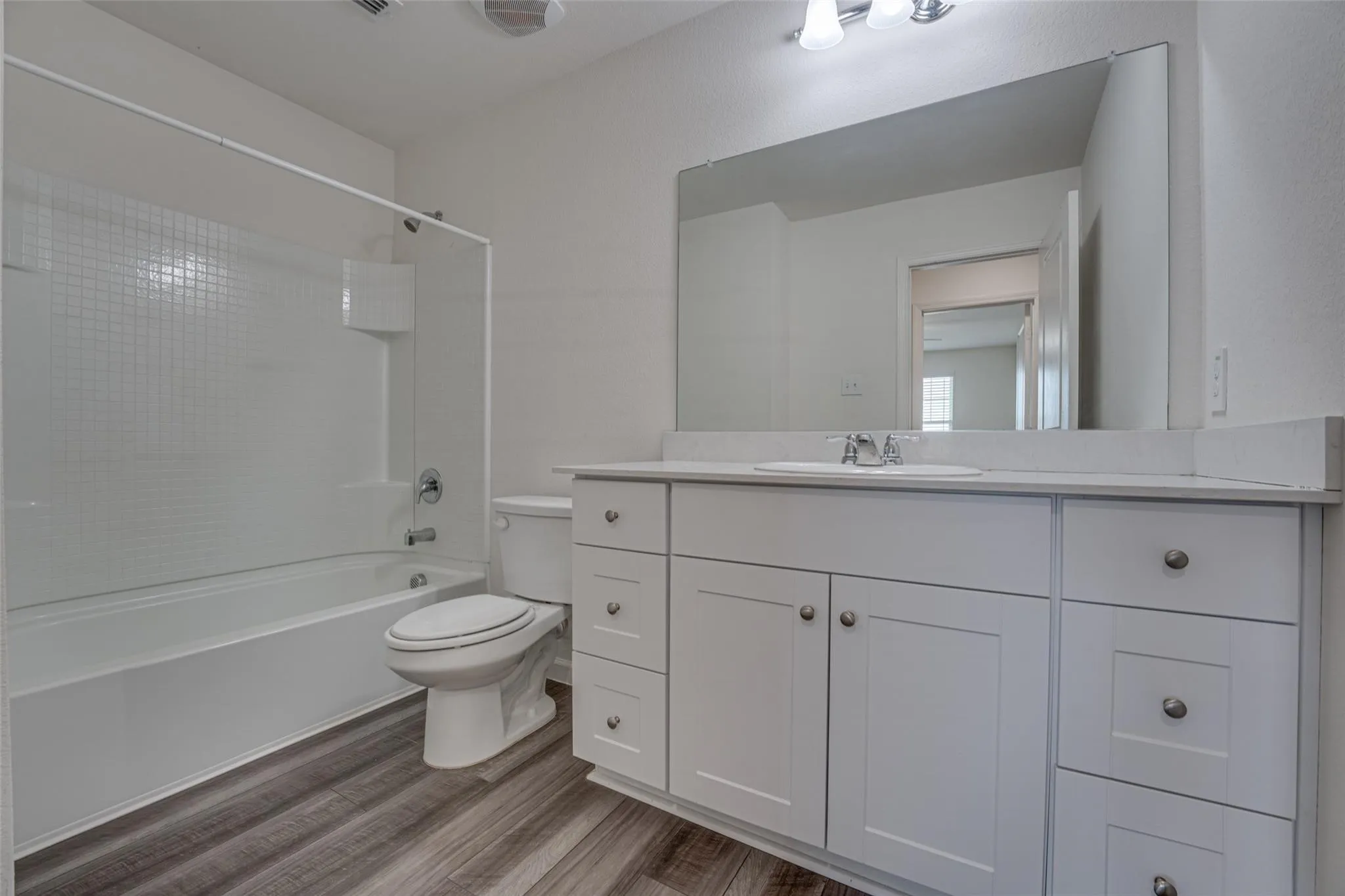 Bathroom featuring a white vanity with panel cabinetry and satin nickel hardware, a white countertop, an integrated sink, a rectangular mirror, and wood-finish flooring