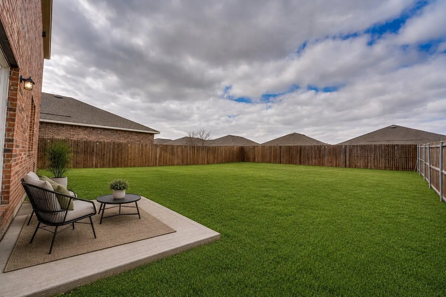 Expansive backyard featuring a manicured lawn, full privacy fencing, and a concrete patio