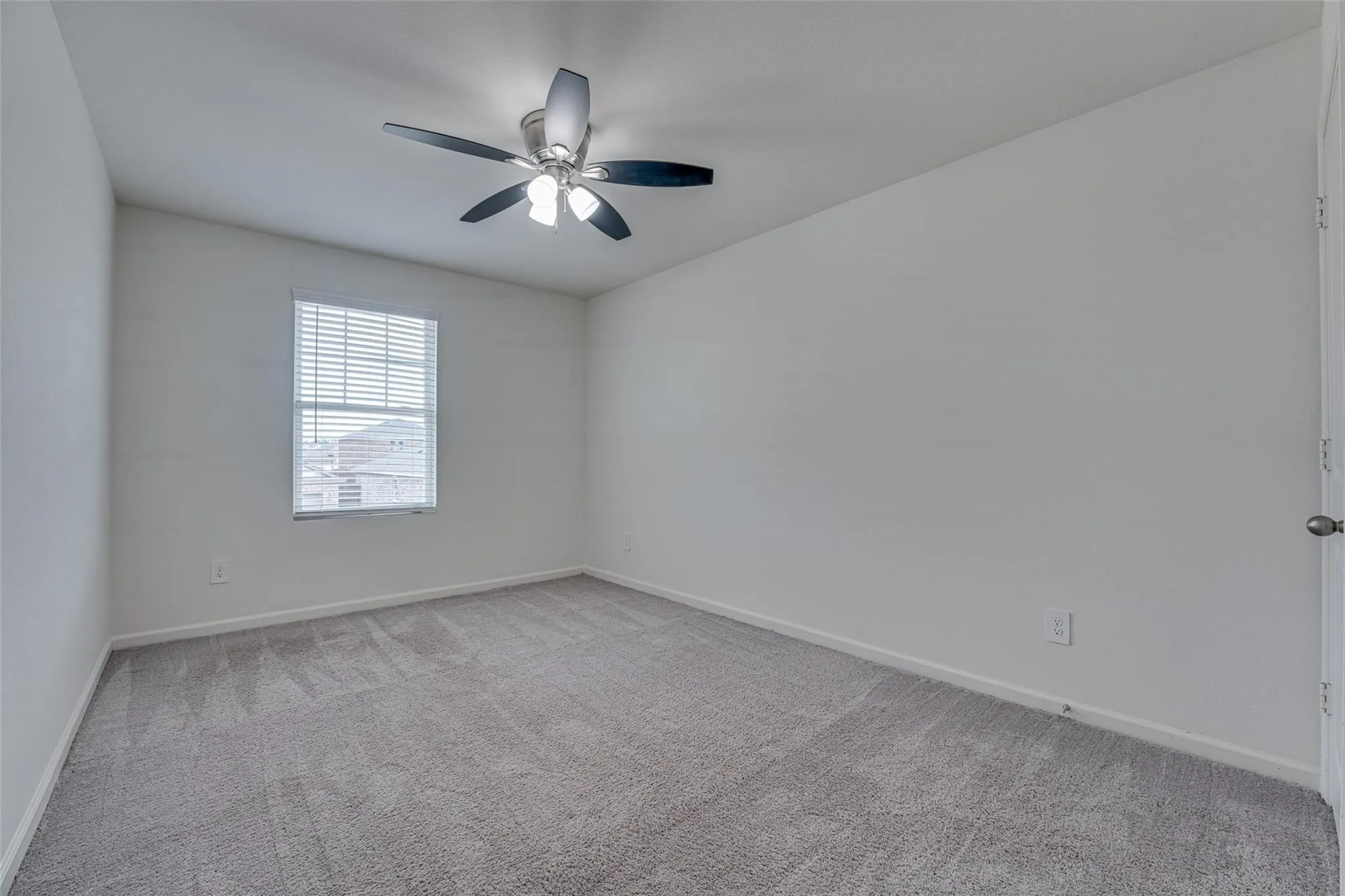 Carpeted room with a ceiling fan light fixture and a window with blinds
