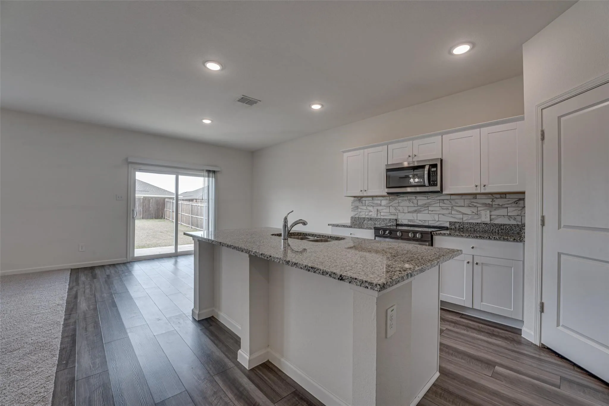 Open-concept living area with wood-finish flooring, recessed lighting, and a sliding glass door to the backyard