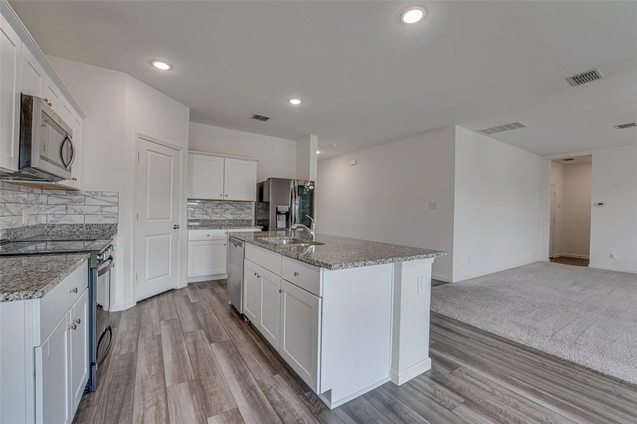 Kitchen featuring white shaker cabinetry, stainless steel appliances, granite countertops, and wood-finish flooring