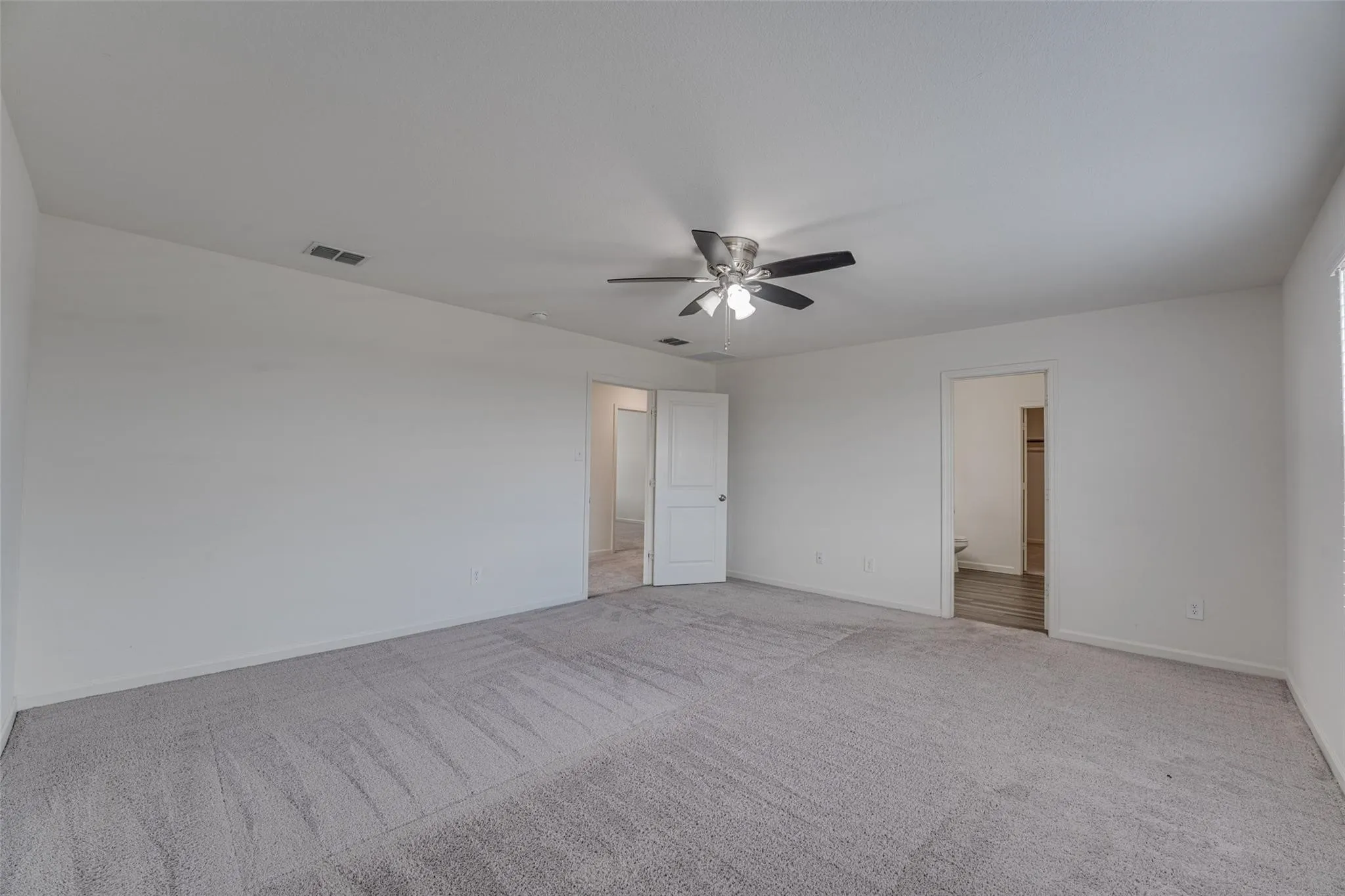 Spacious carpeted room featuring a ceiling fan with integrated lighting and multiple doorways