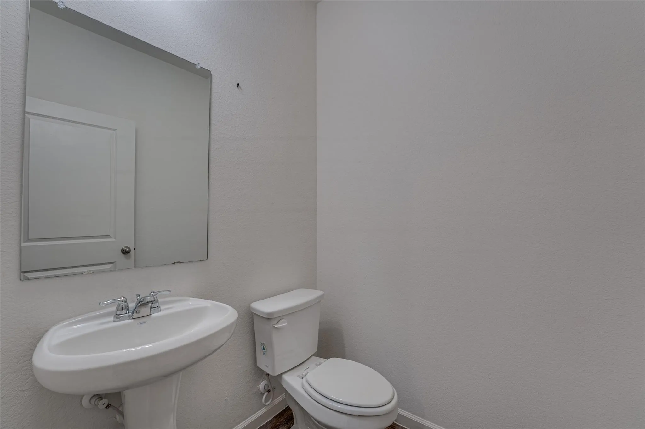 Pedestal sink with chrome fixtures, wall-mounted mirror, and white toilet
