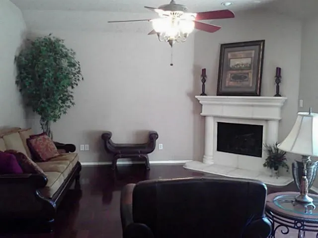 Fireplace with a white mantel and hearth, dark wood-finish flooring, and a ceiling fan with integrated lighting