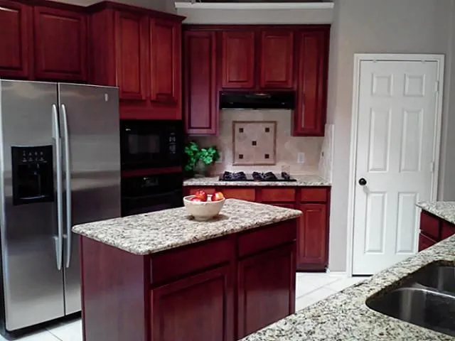 Elegant kitchen featuring rich burgundy cabinetry, speckled stone countertops throughout, stainless steel appliances including a side-by-side refrigerator, and a spacious island with seating