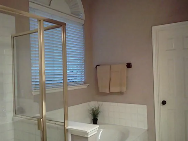 Built-in bathtub with tiled surround, shower enclosure with glass panels, arched transom window, and paneled door