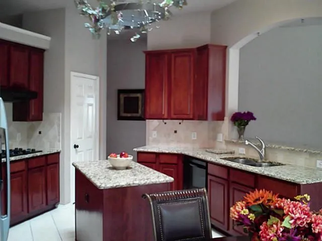 Kitchen featuring wood-finish cabinetry, light-toned granite countertops, a center island, and a stainless steel sink with a high-arc faucet