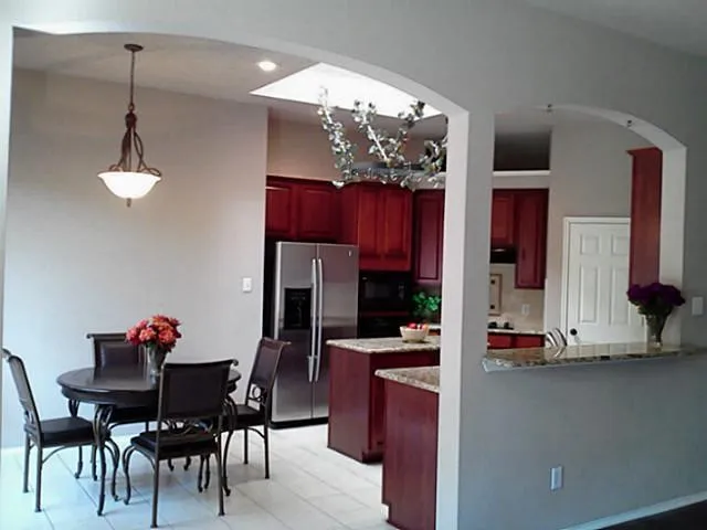 Arched doorways opening to a kitchen with rich wood cabinetry, stainless steel appliances, granite countertops, and a skylight