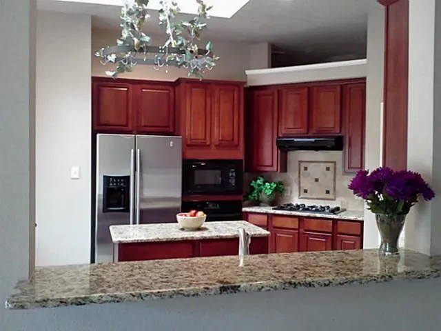 Kitchen featuring wood cabinetry, stainless steel appliances, granite countertops, and a tiled backsplash