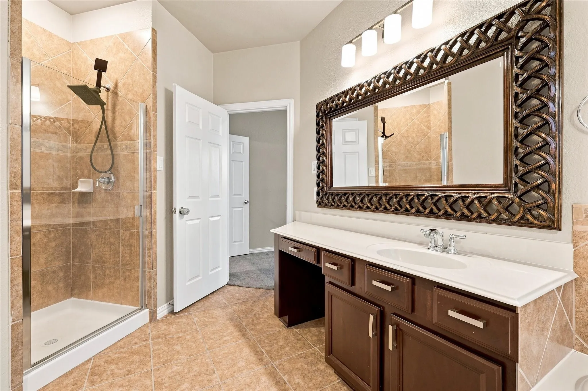 Walk-in shower with tiled surround, wood-finish vanity with built-in storage, white countertop, and an ornate framed mirror