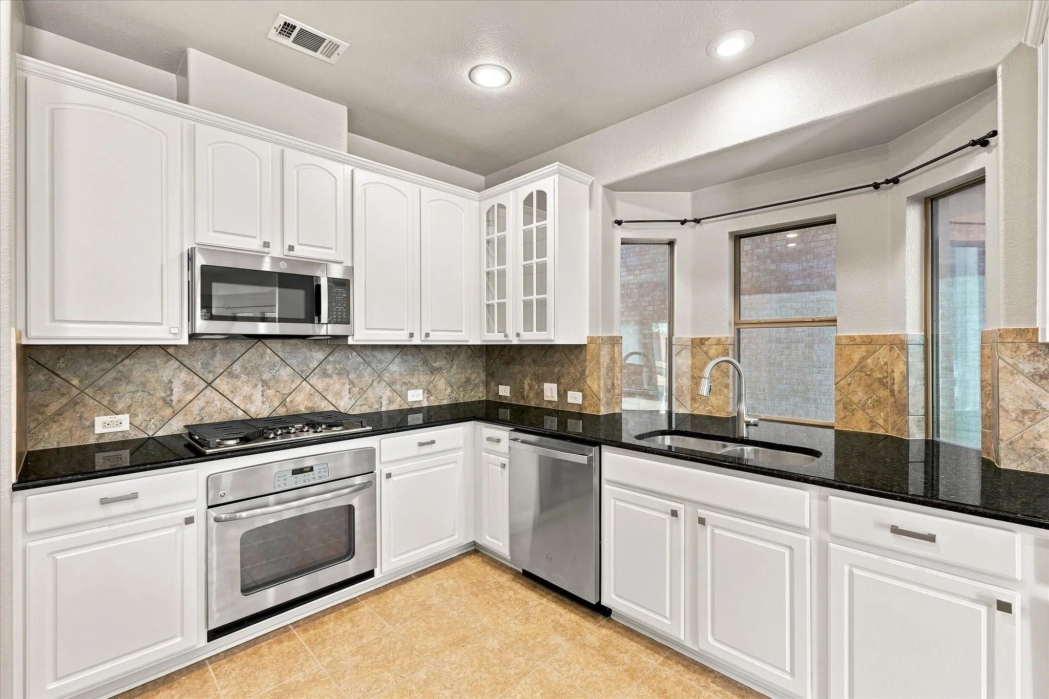 Kitchen featuring white cabinetry, black countertops, stainless steel appliances, and a tiled backsplash