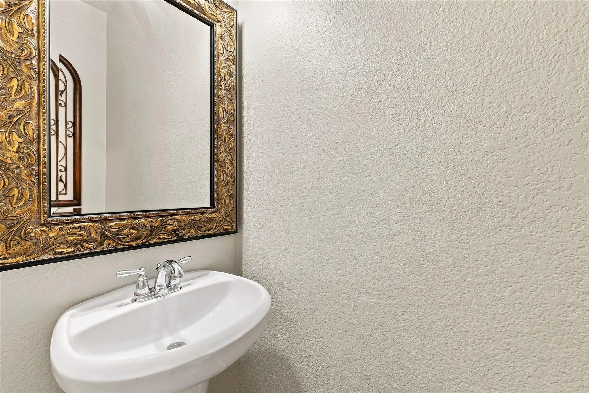 Pedestal sink with chrome-finish faucet and an ornate framed mirror