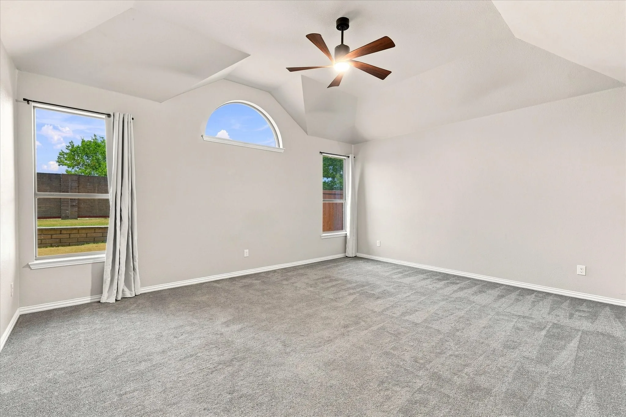 Spacious room featuring vaulted ceilings, a ceiling fan with light, and light gray wall paint