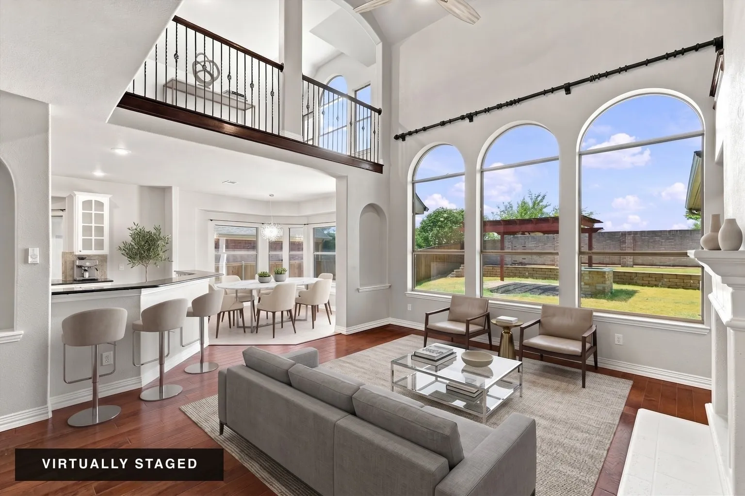 Two-story living area featuring wood-finish flooring, a white mantel, and three arched windows