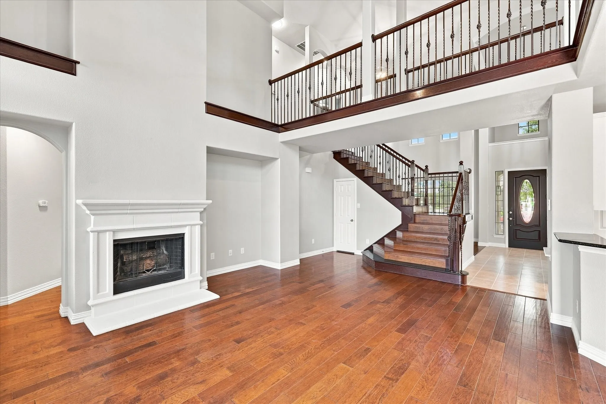 Two-story living space featuring wood-finish flooring, a white mantel fireplace, and a grand staircase with wrought iron balusters