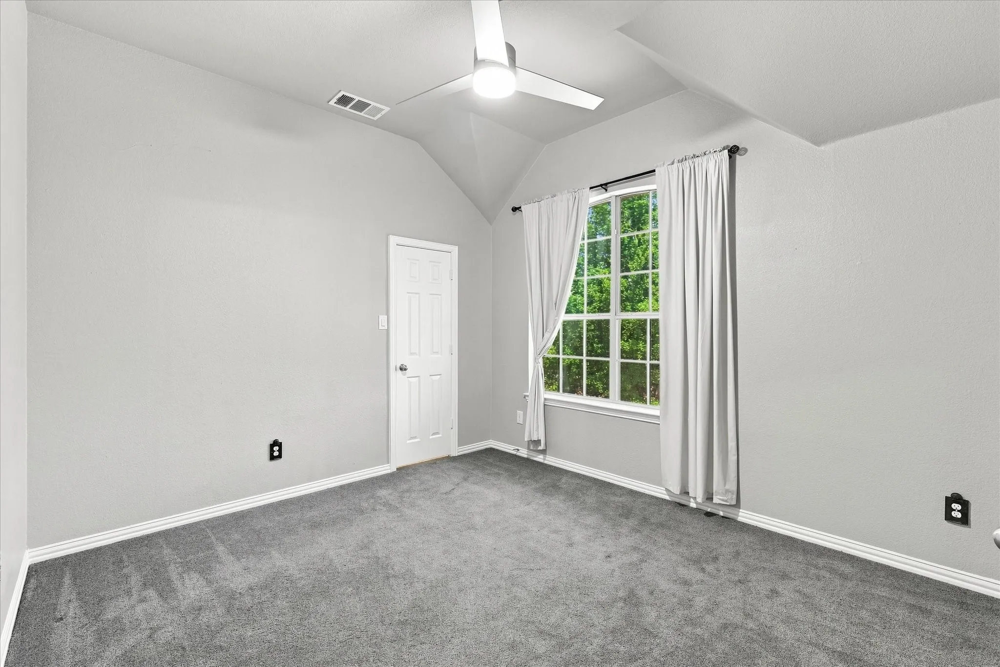 Spacious room featuring vaulted ceilings, a ceiling fan, a paneled door, and a large window