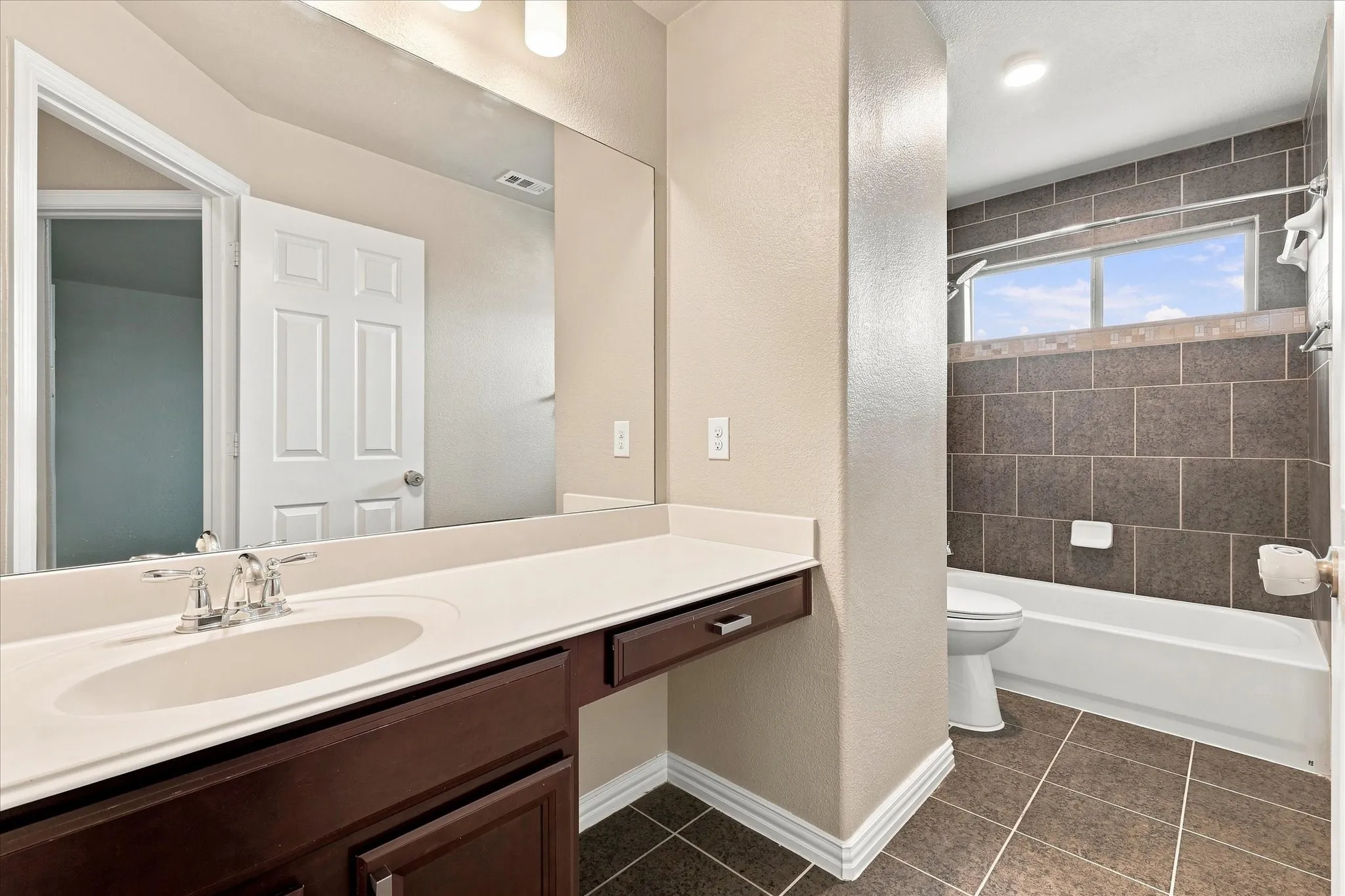 Dark wood-finish vanity with a single basin, expansive mirror, and white countertop