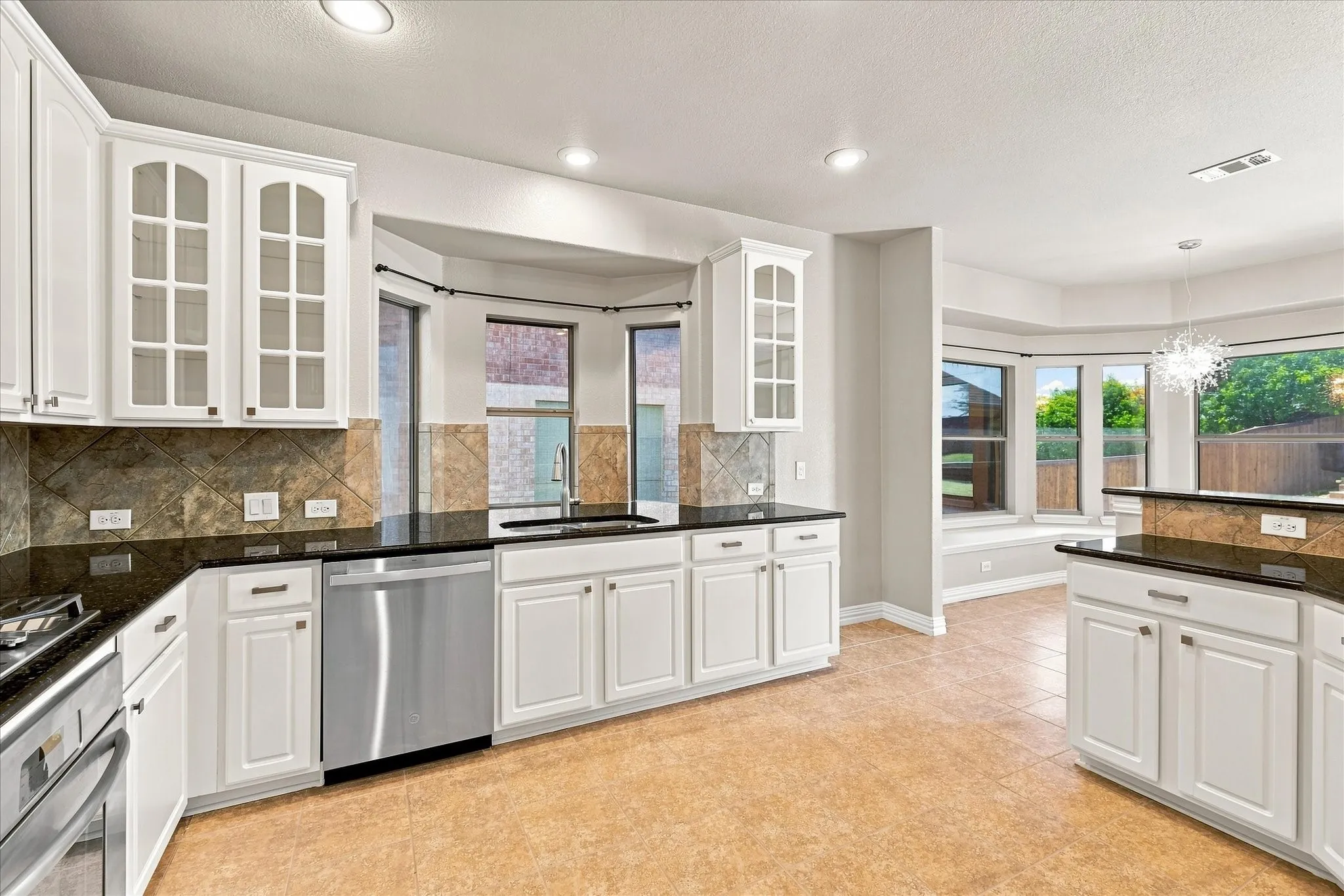 White cabinetry, stainless steel appliances, black countertops, tile backsplash, and recessed lighting