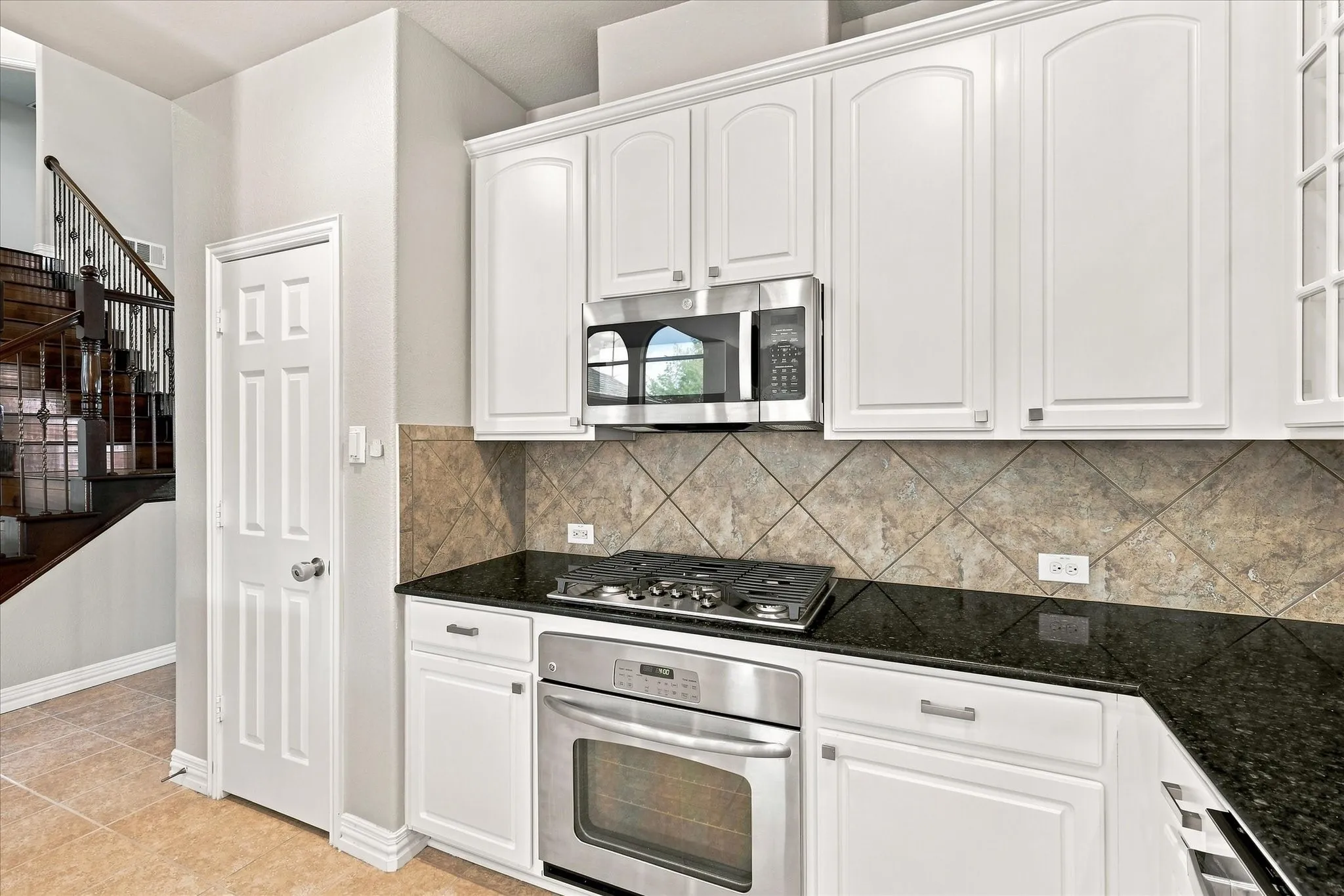 White cabinetry with stainless steel appliances, dark countertop, and diagonally set tile backsplash