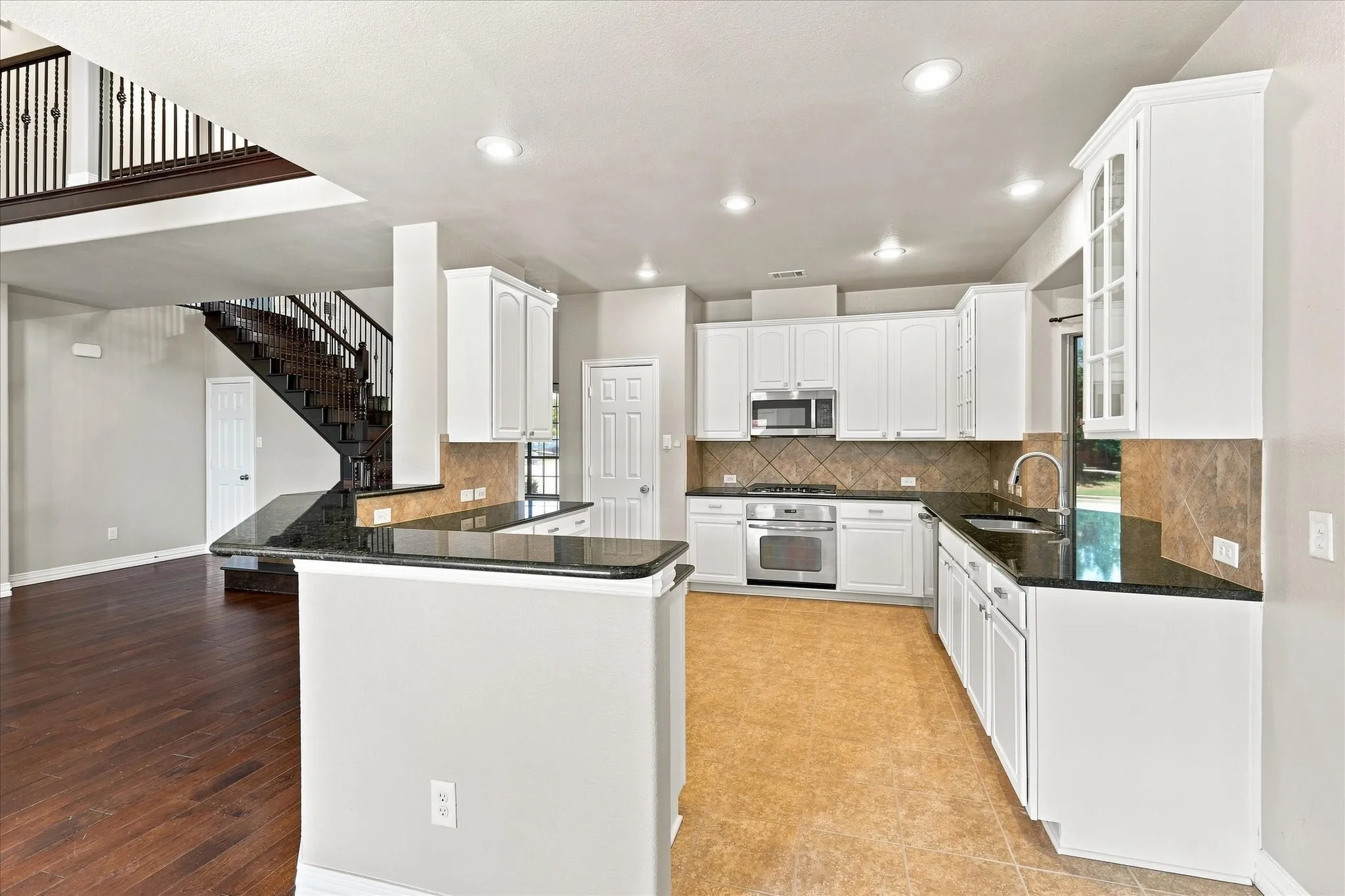 White cabinetry with glass-front accents, dark stone countertops, stainless steel appliances, tile backsplash, and dark wood-finish flooring