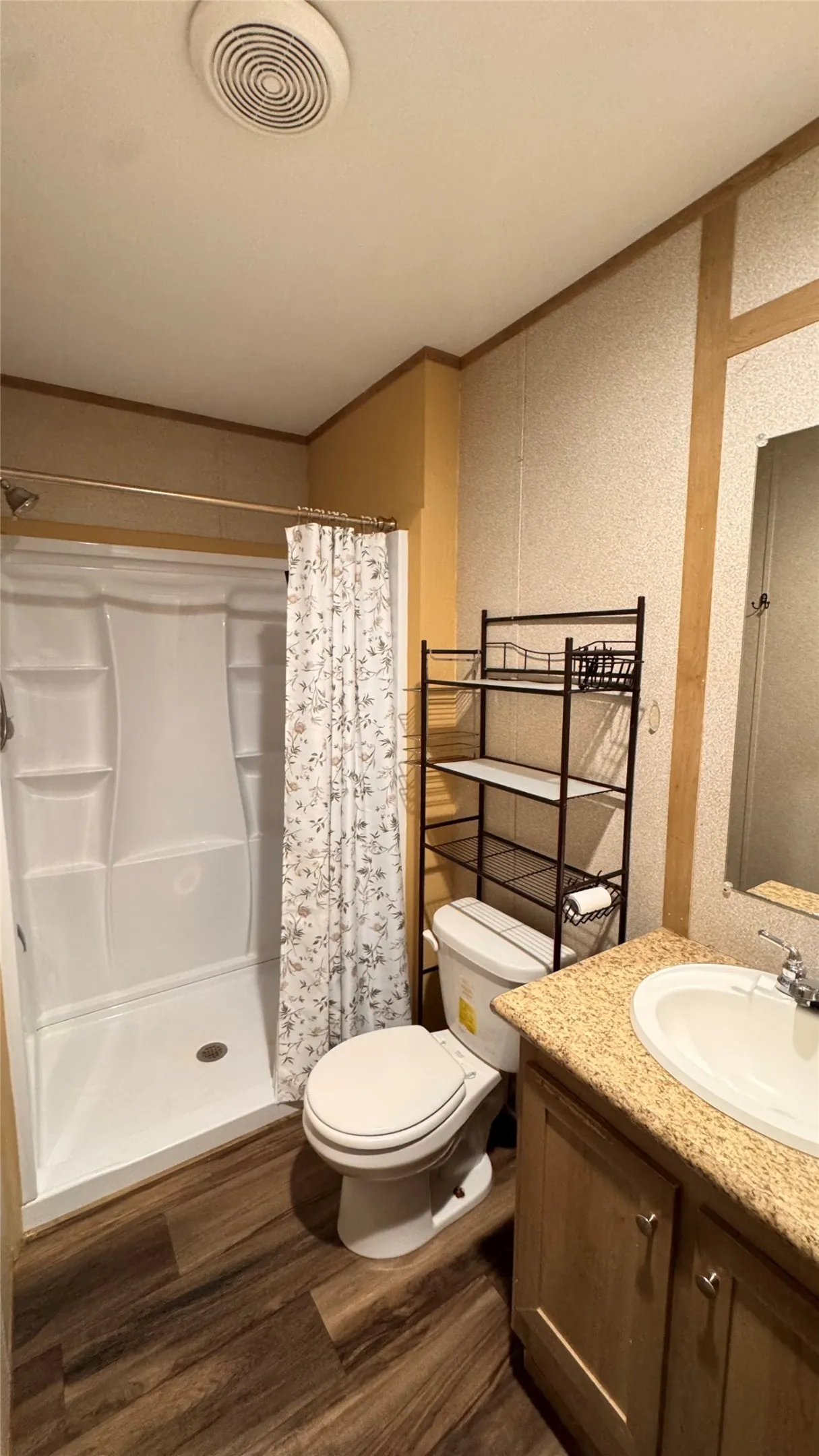 Wood-finish flooring, white shower stall, vanity with integrated sink, and a framed mirror
