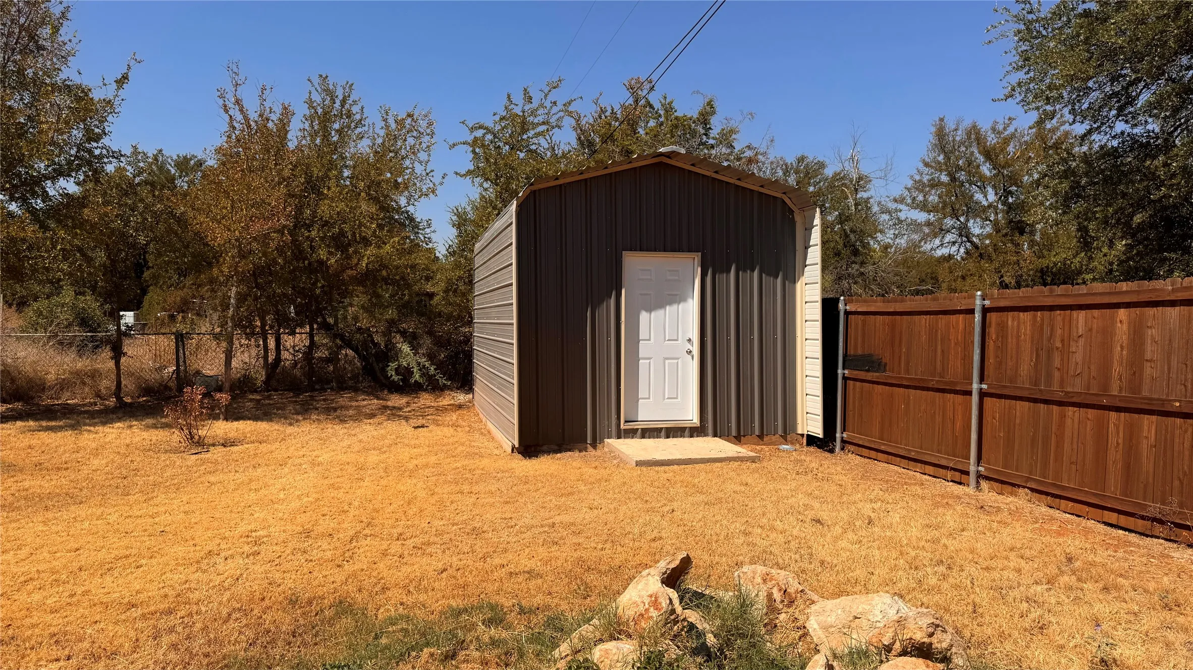 Metal storage building with a white entry door, positioned on a concrete pad