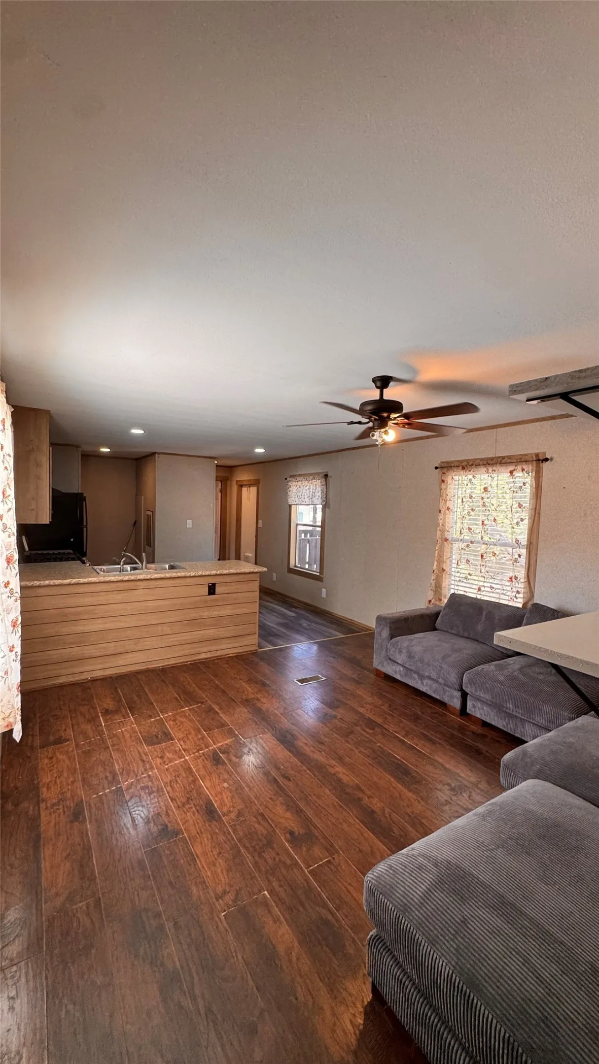 Wood-finish flooring throughout, with a ceiling fan in the living area and recessed lighting in the kitchen