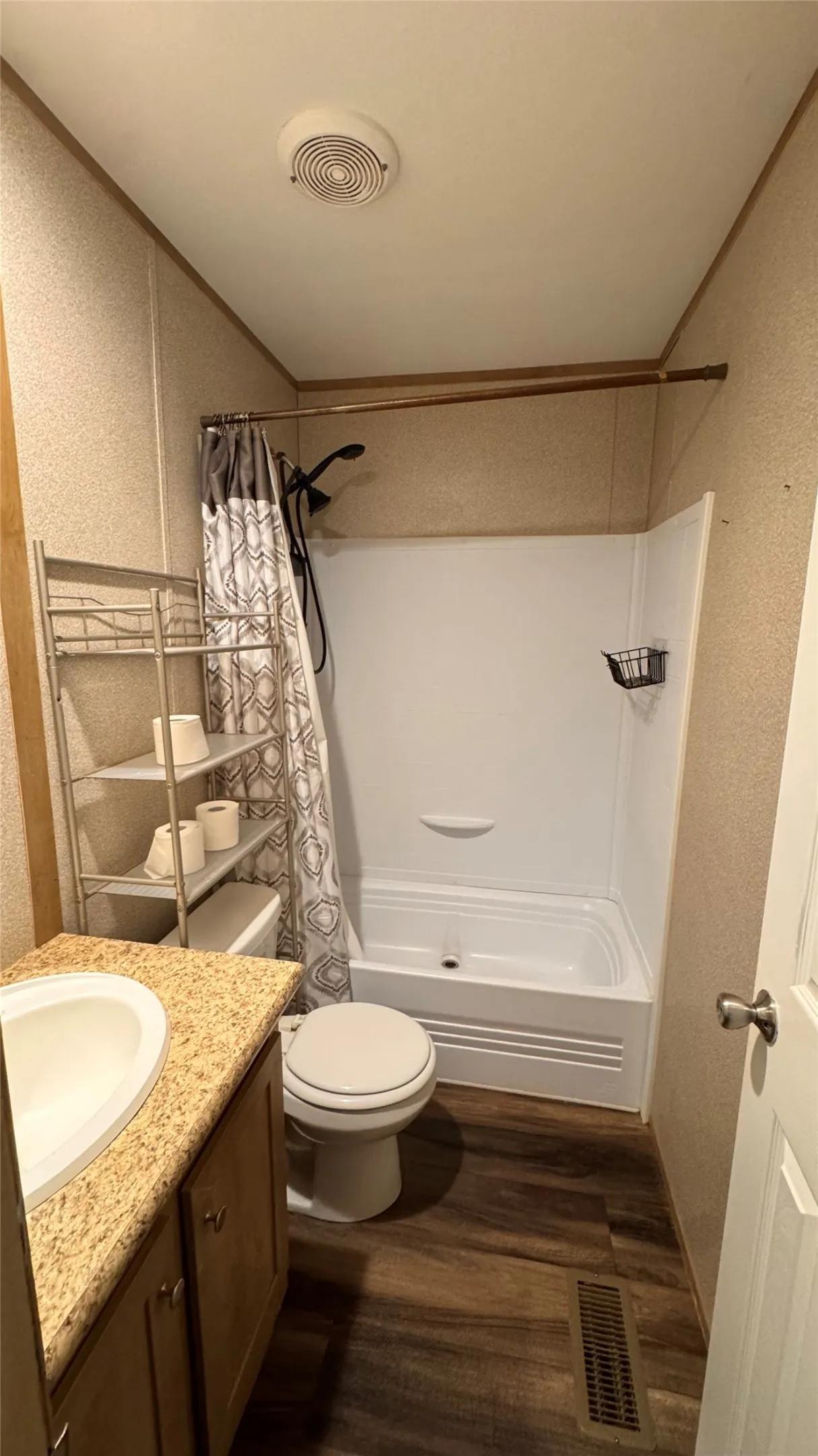 Bathroom with wood-finish flooring, white bathtub with shower, white toilet, and vanity with an integrated sink and light-toned countertop