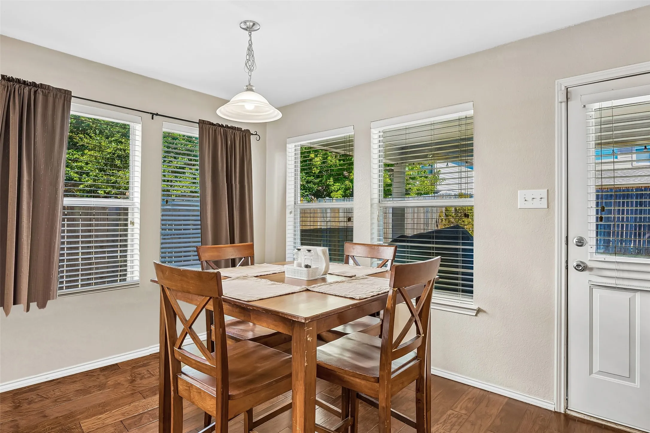 Warm interior with wood-finish flooring, multiple windows, a ceiling-mounted light fixture, and a white paneled door with an integrated window