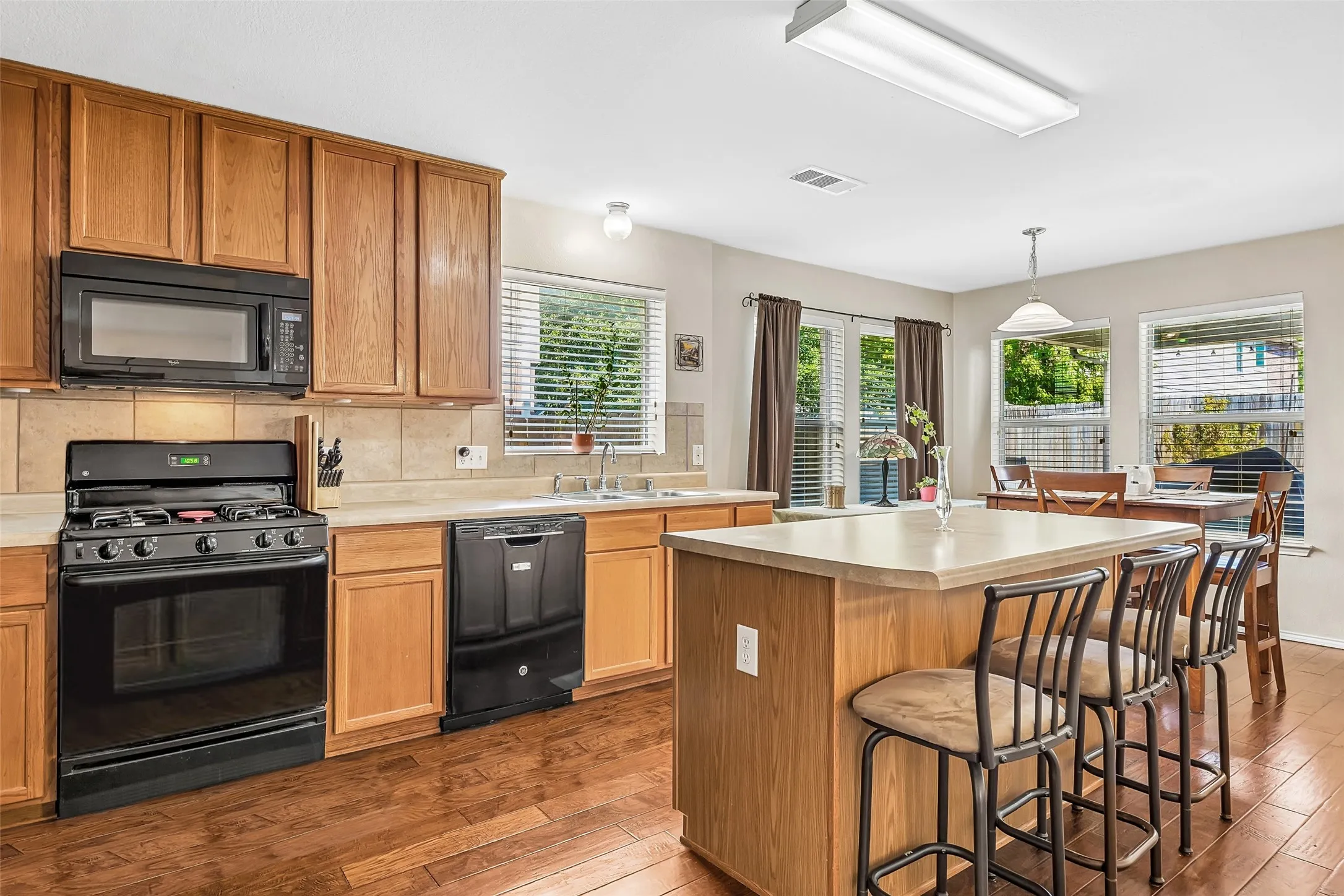 Kitchen featuring wood-finish flooring, wood cabinetry, a center island with countertop seating, and black appliances