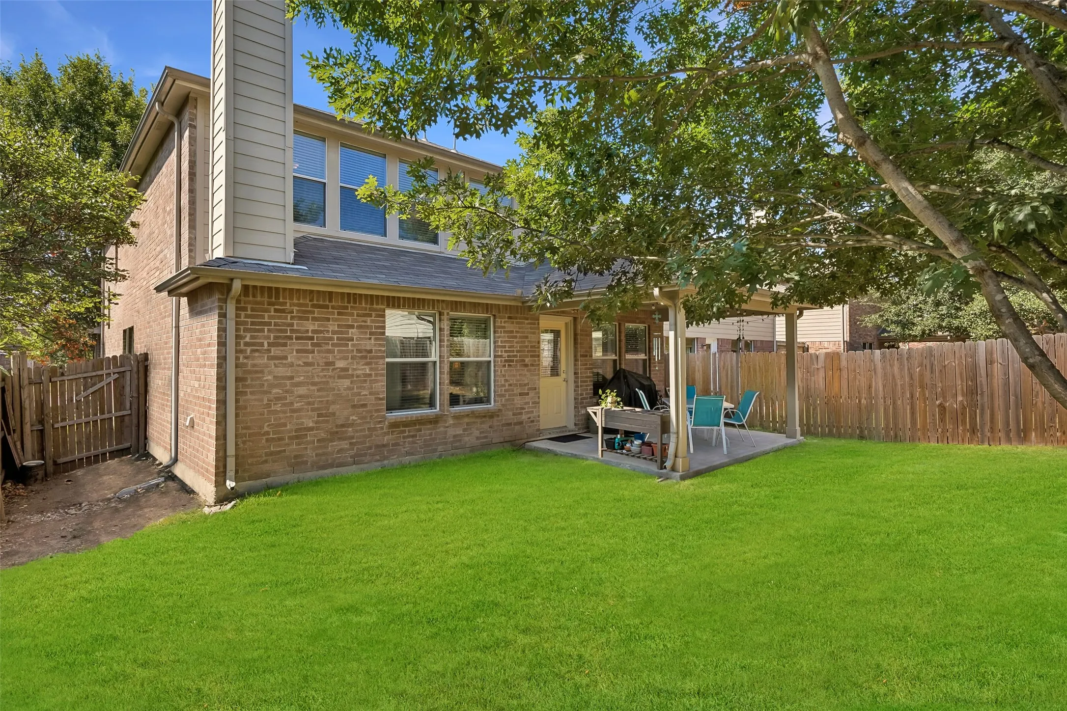 Expansive green lawn with a covered patio, full brick exterior, and a privacy fence