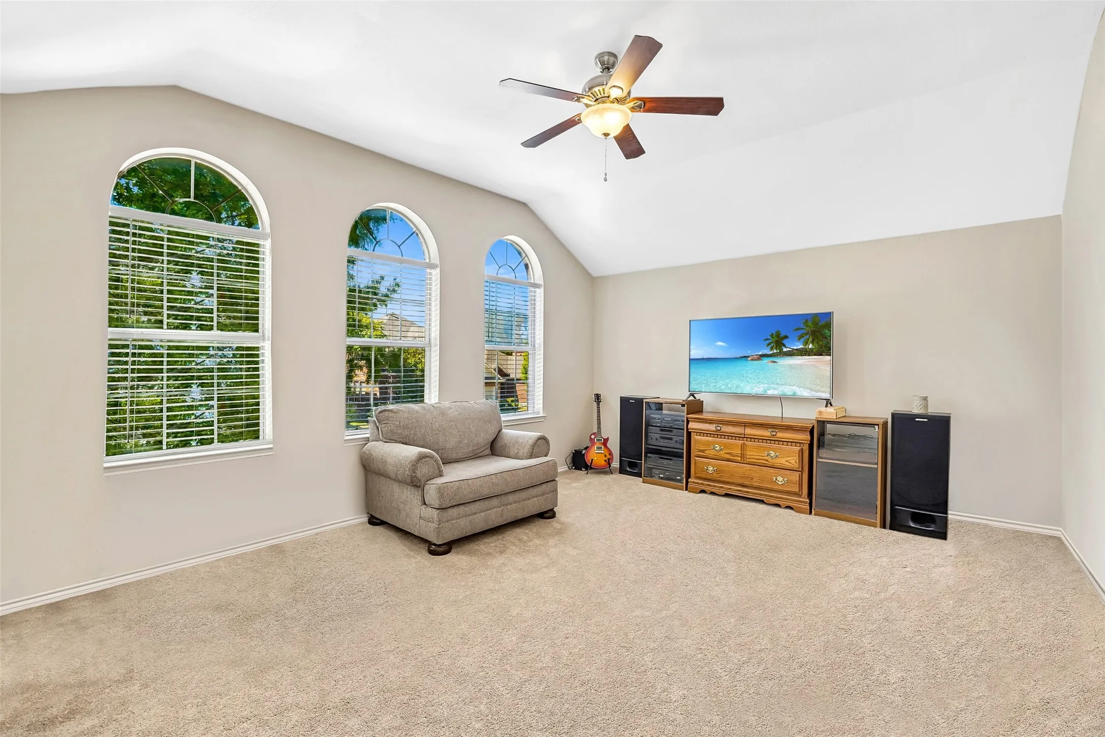 Vaulted ceilings with a ceiling fan, three arched windows, and light neutral carpeting