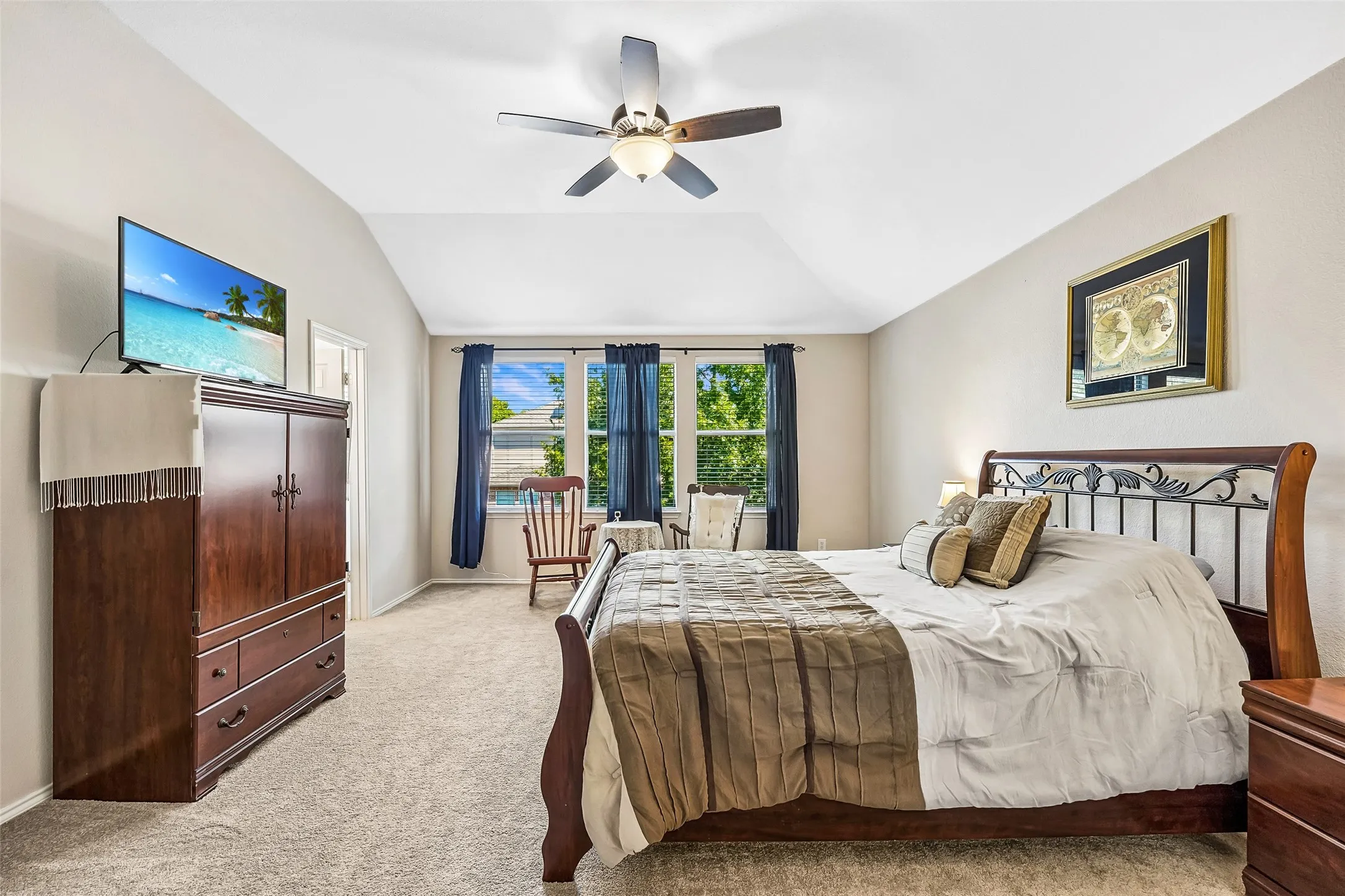 Vaulted ceiling with a ceiling fan, carpeted flooring, and a large window with blue curtains
