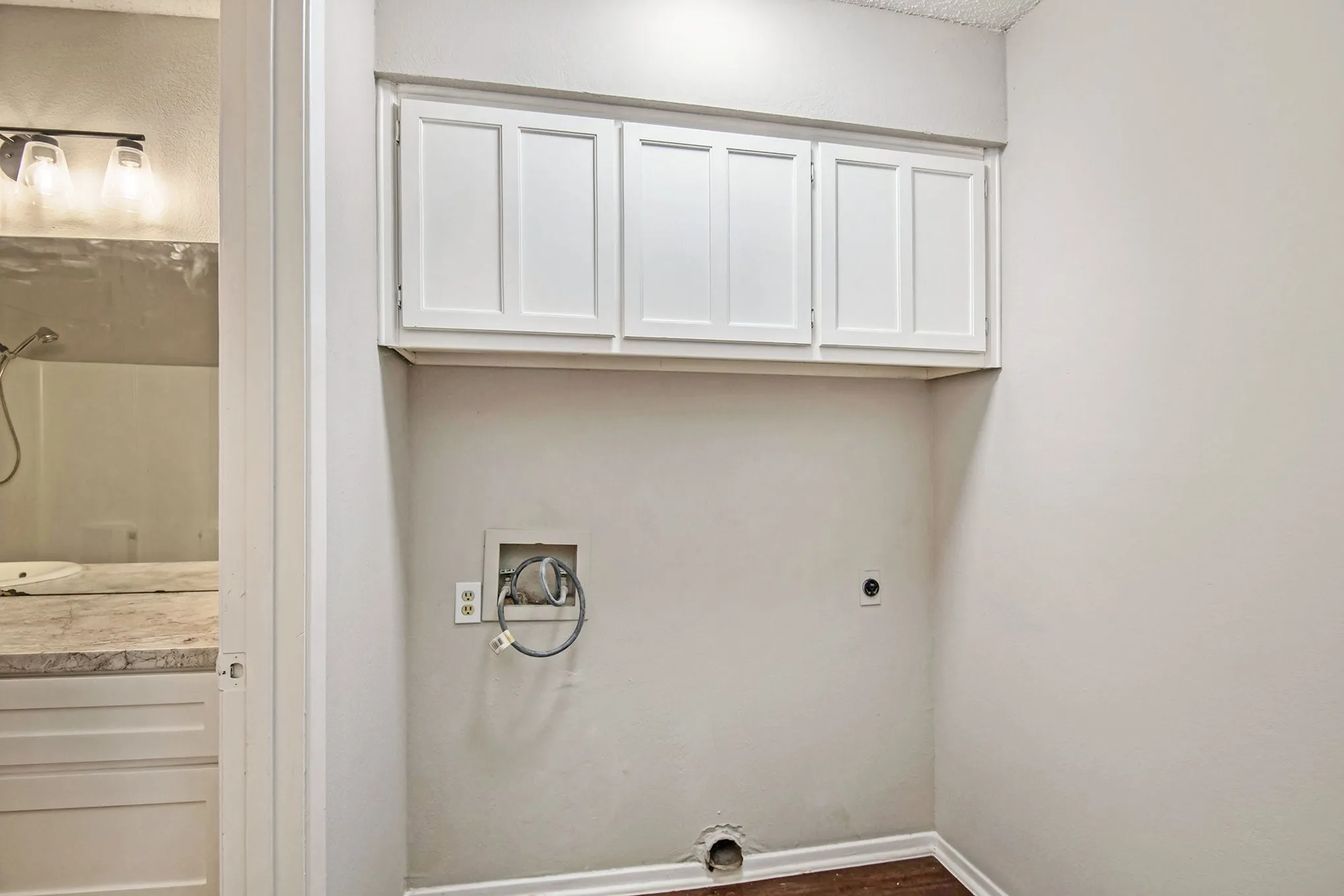 Laundry area with overhead white cabinetry, wood-finish flooring, and light-toned walls