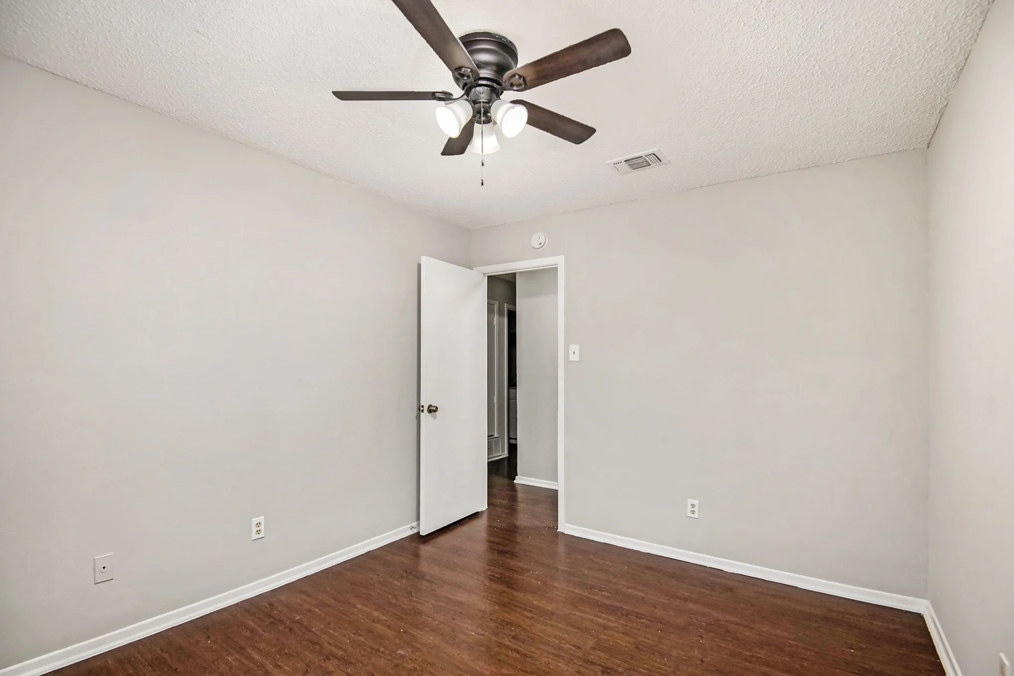 Wood-finish flooring, light neutral wall paint, and a ceiling fan with integrated lighting