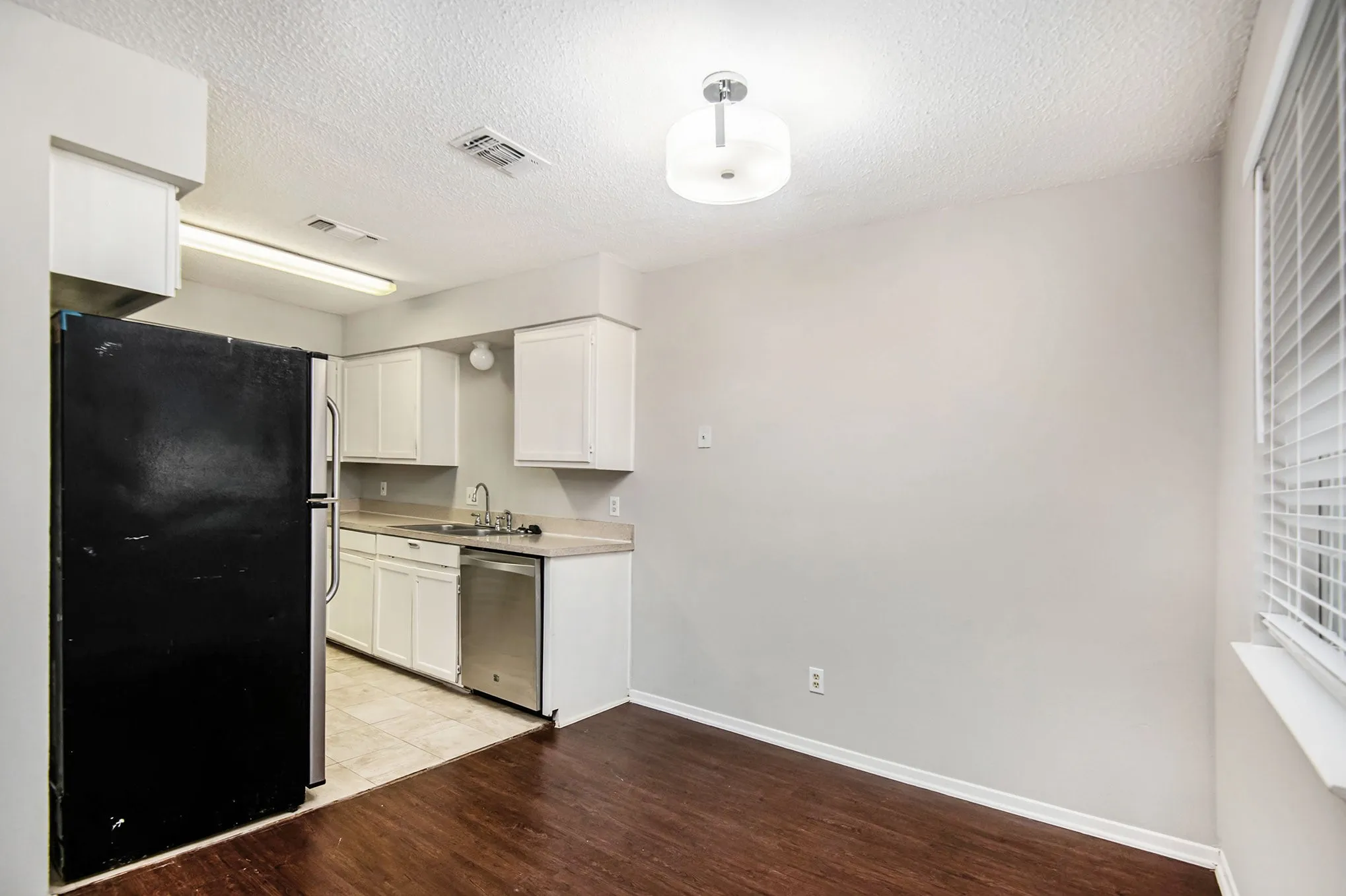 Kitchen and dining area featuring wood-finish flooring, white cabinetry, a stainless steel dishwasher, and a window with blinds