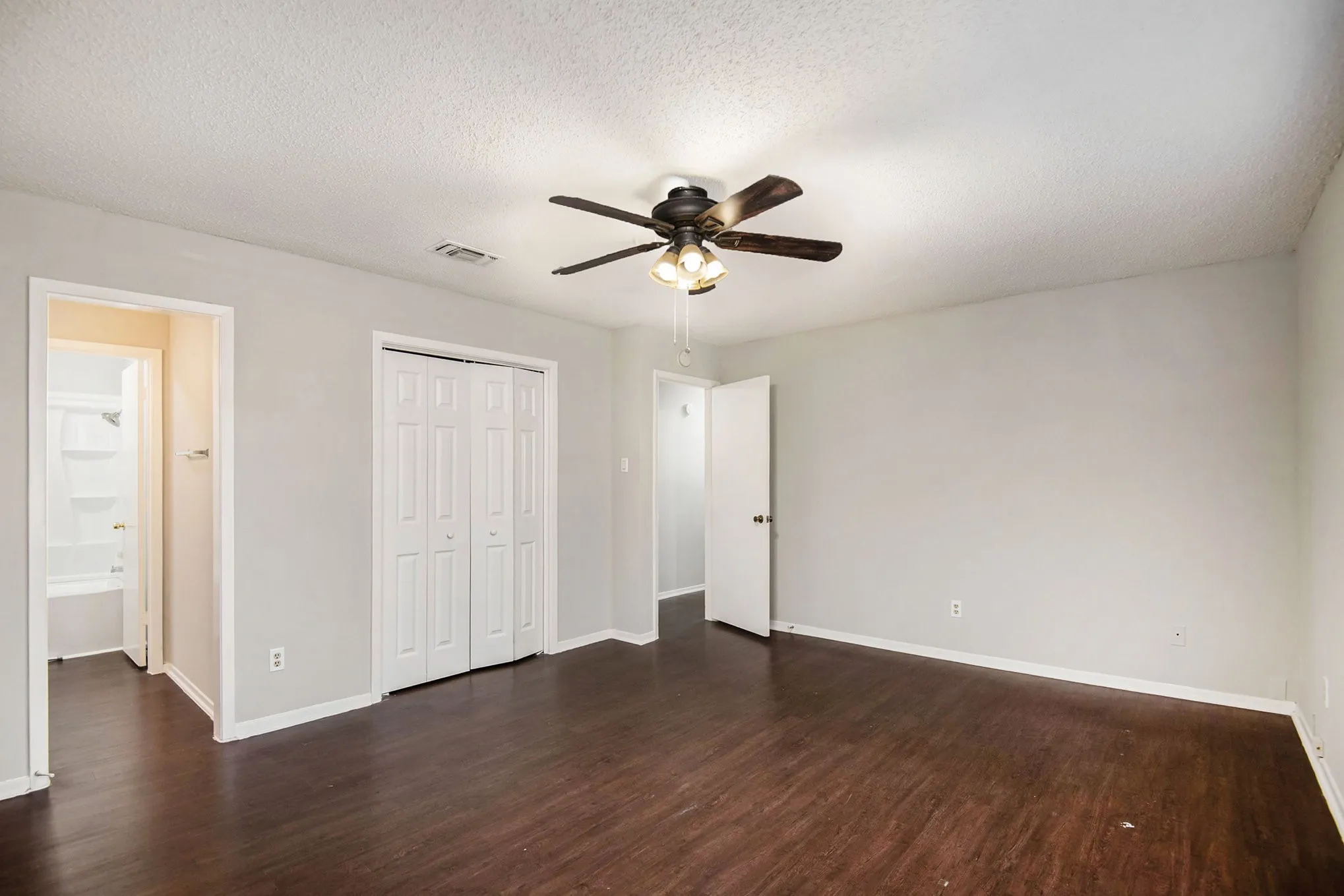 Spacious room with wood-finish flooring, light gray walls, and a ceiling fan with light fixture