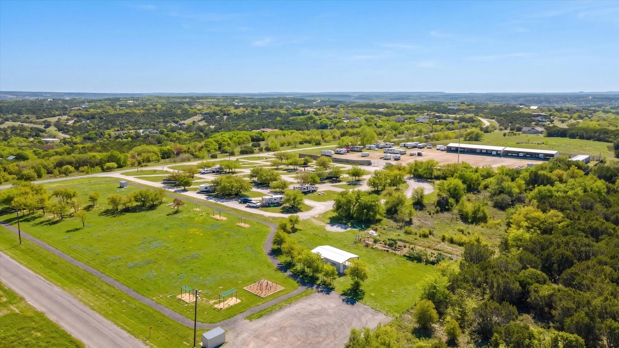 Expansive property featuring multiple RV parking sites, paved driveways, a large metal structure, and a covered open-air structure, all surrounded by mature trees and natural landscaping