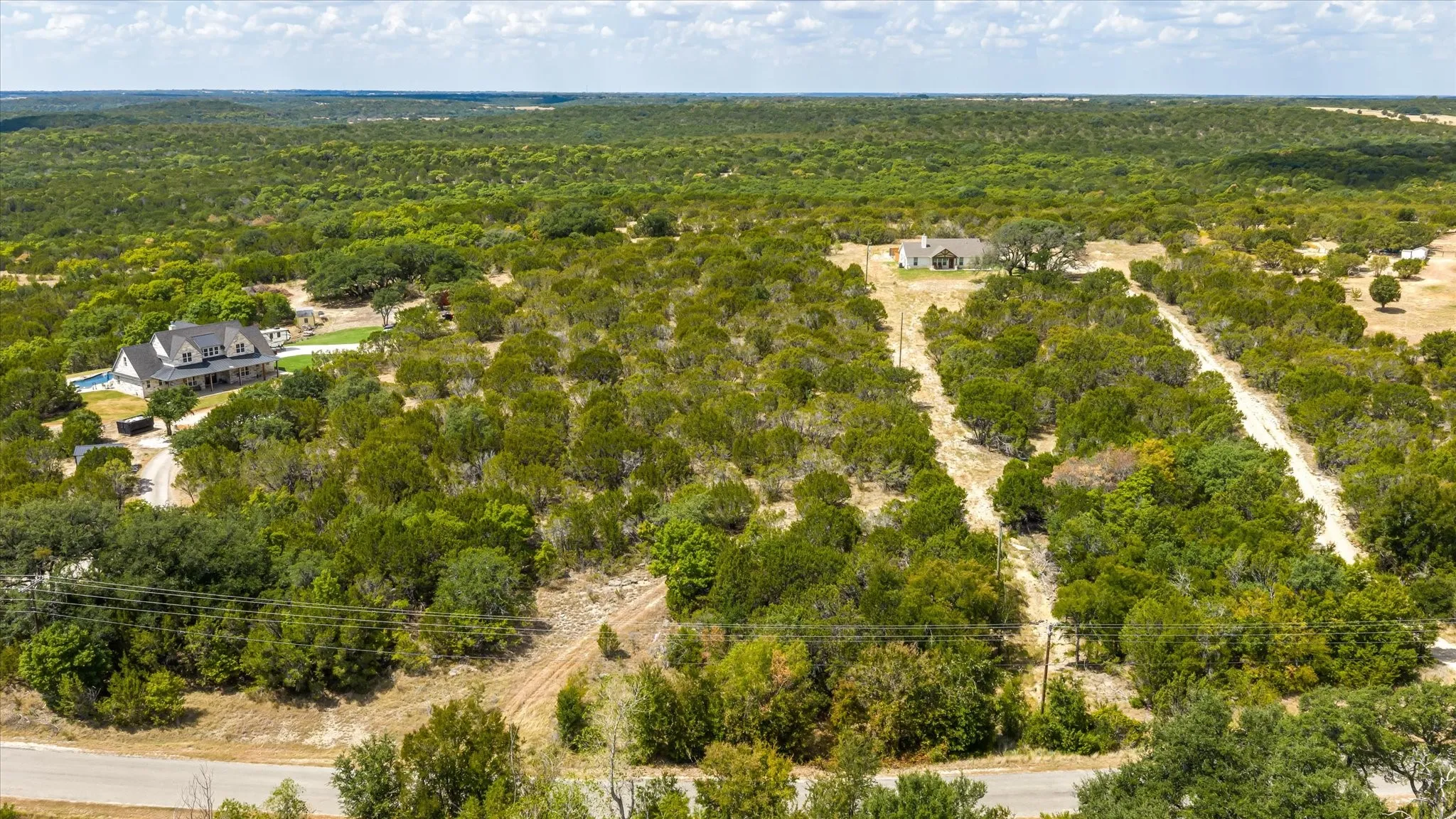 Expansive treed landscape with residential structures and unpaved access paths
