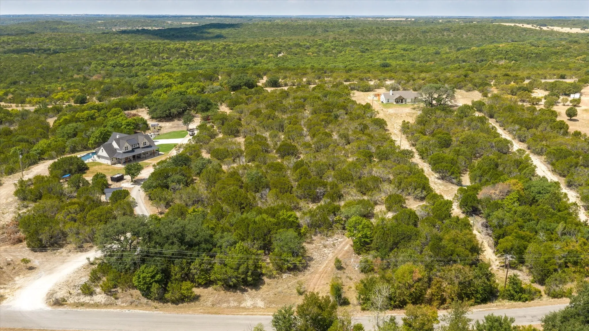 Expansive natural landscaping with mature trees, a winding gravel driveway, and a distant residence with a visible roofline