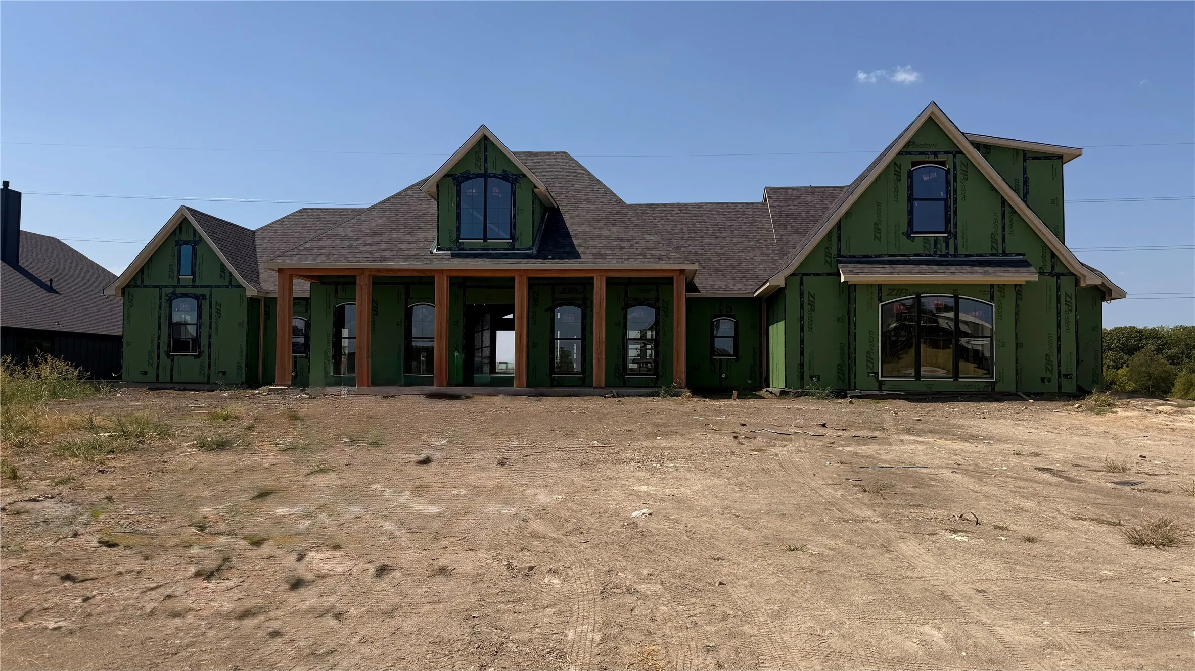 New construction home featuring a covered front porch with wood columns, an arched window, and a gabled roofline