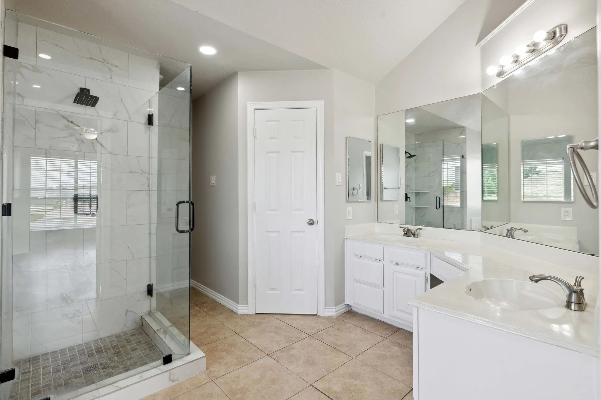 Bathroom featuring a shower with door, a wealth of natural light, oversized vanity, vaulted ceiling, and dual sinks