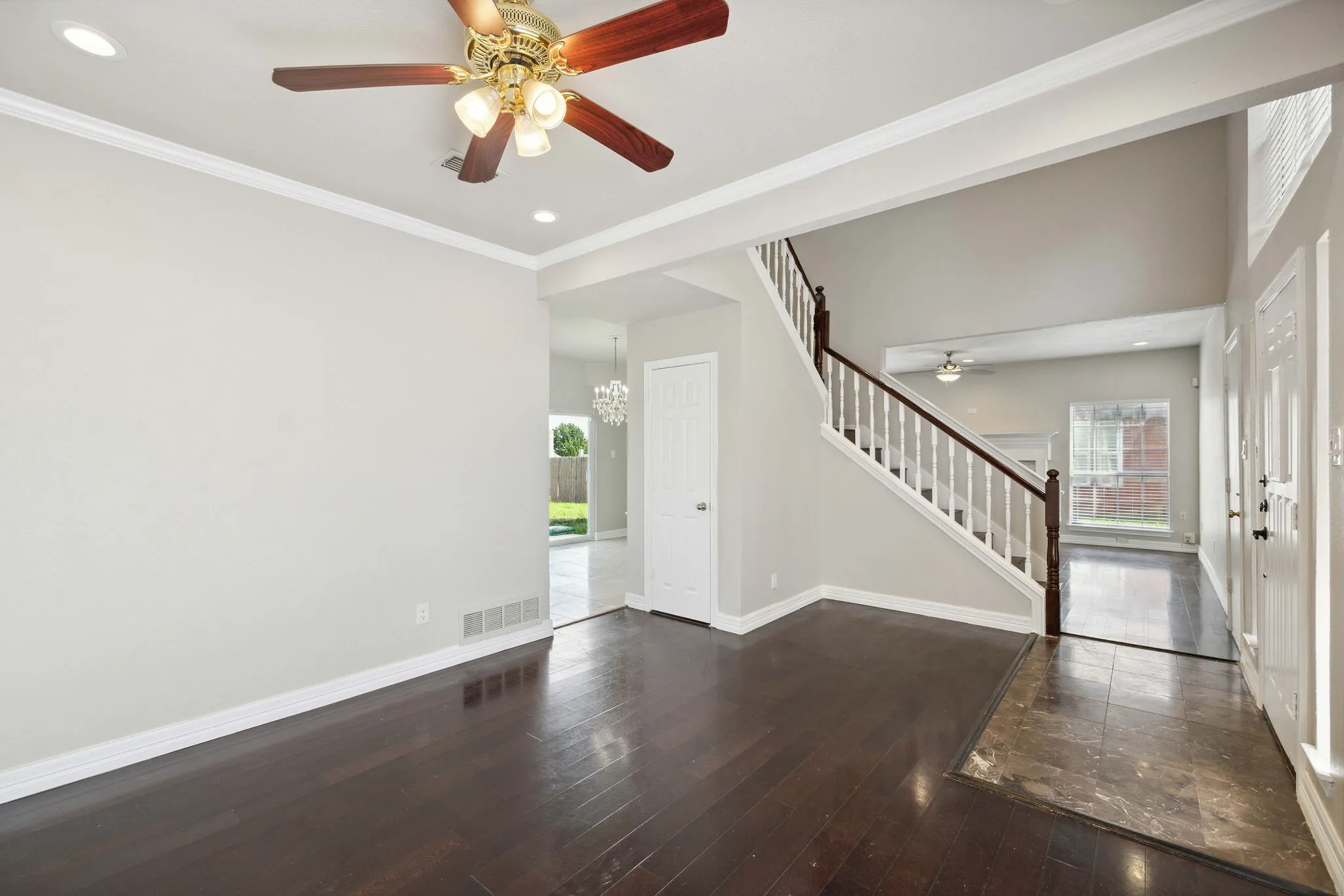 Empty room featuring dark hardwood / wood-style flooring, ceiling fan with notable chandelier, and crown molding