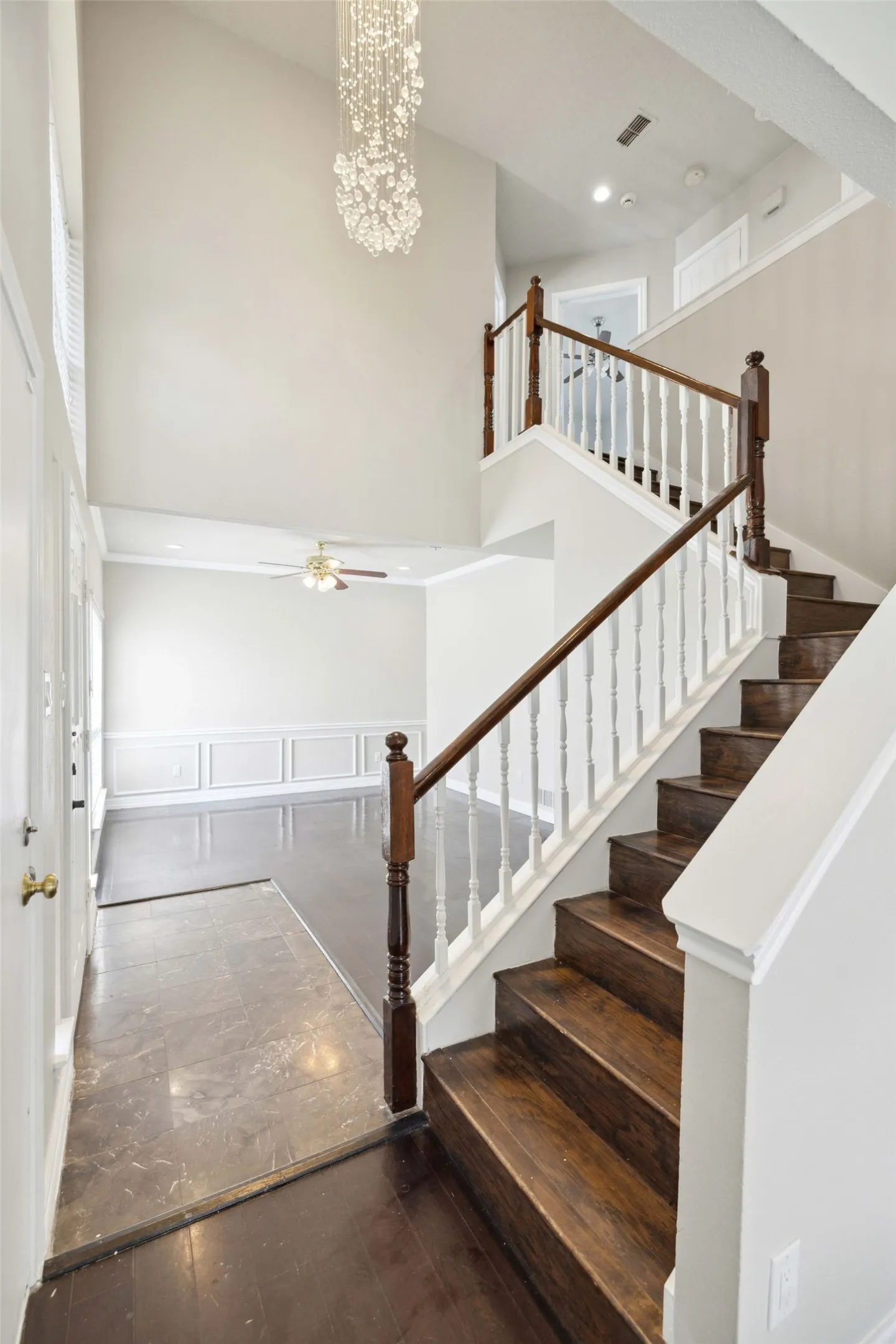 Stairway with ceiling fan with notable chandelier, dark wood-type flooring, and a high ceiling